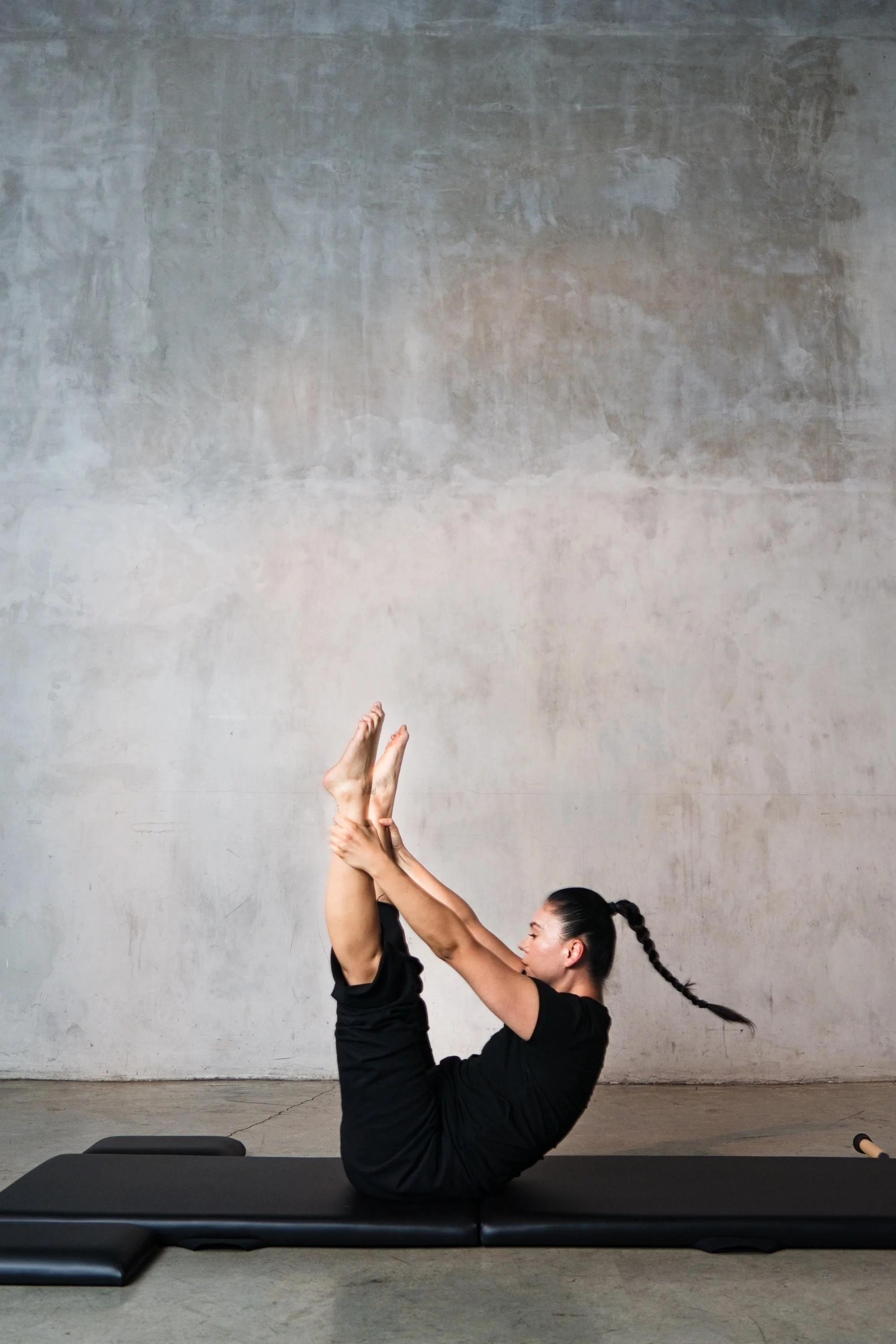 A woman demonstrating classical Pilates exercise Open Leg Rocker on a Gratz Low Folding Mat.
