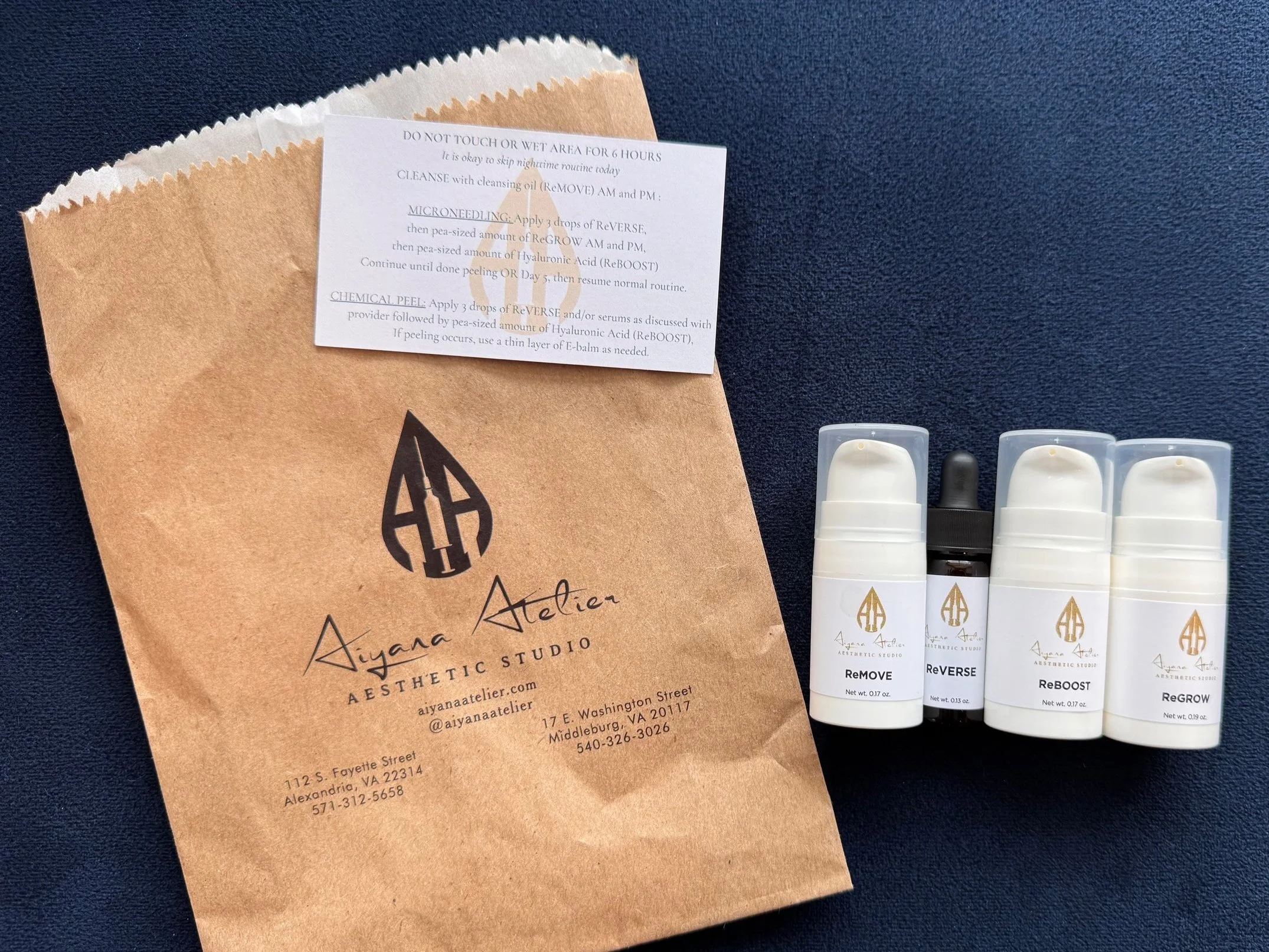 A paper bag from Aiyana Atelier with a logo design, a sheet of skincare instructions, and four small bottles labeled ReMOVE, ReVERSE, ReBOOST, and ReGROW on a dark textured background.