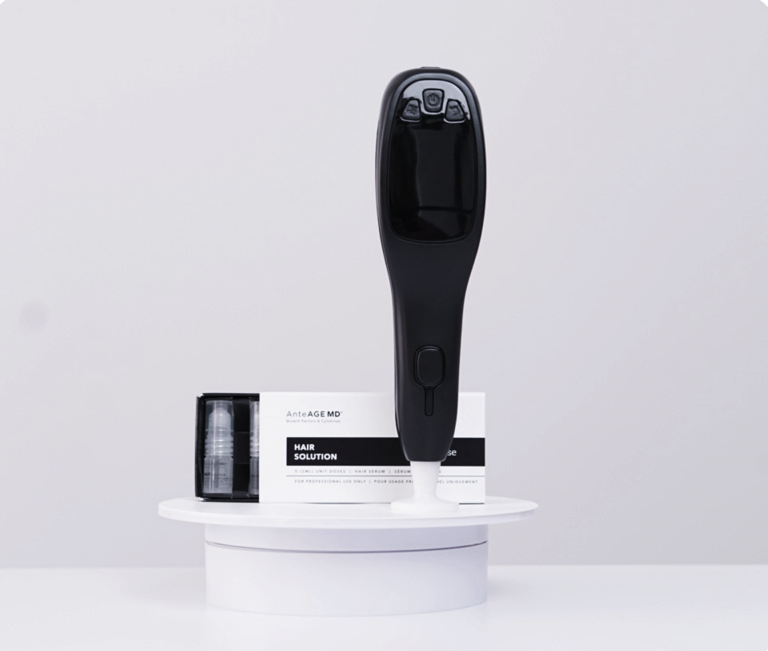 A black handheld device with a digital screen and control buttons stands on a white pedestal, with hair serum and additional product packaging labeled 'AnteAGE MD' on a white surface against a plain white background.