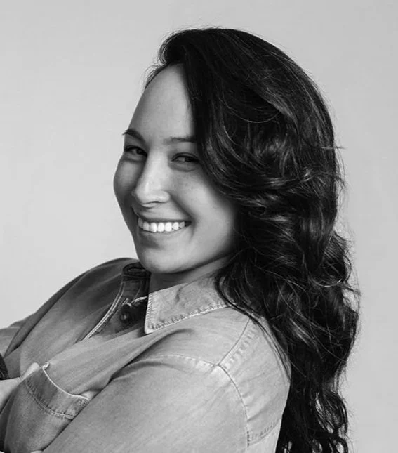 Black and white portrait of a smiling woman with long wavy hair, wearing a denim shirt.