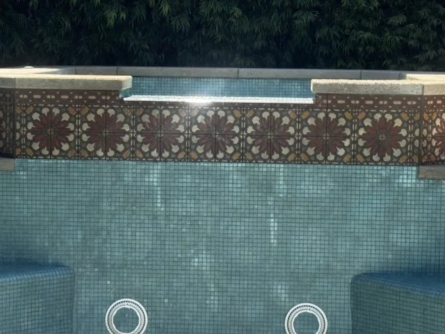 Empty swimming pool with tiled interior and a decorative tiled wall at the edge.