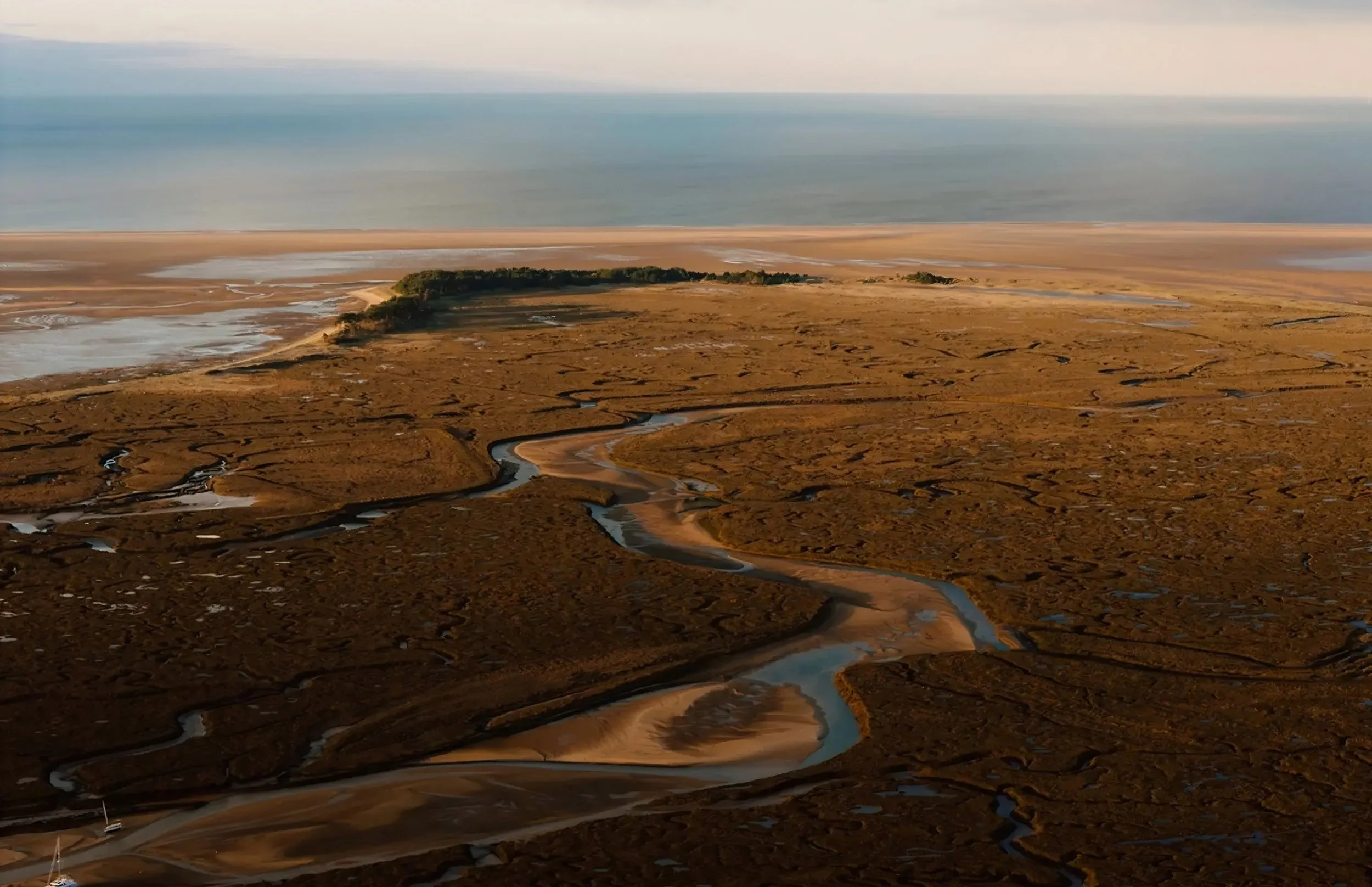 Aerial view of a coastal landscape with marshes, waterways, and a distant shoreline along the sea.