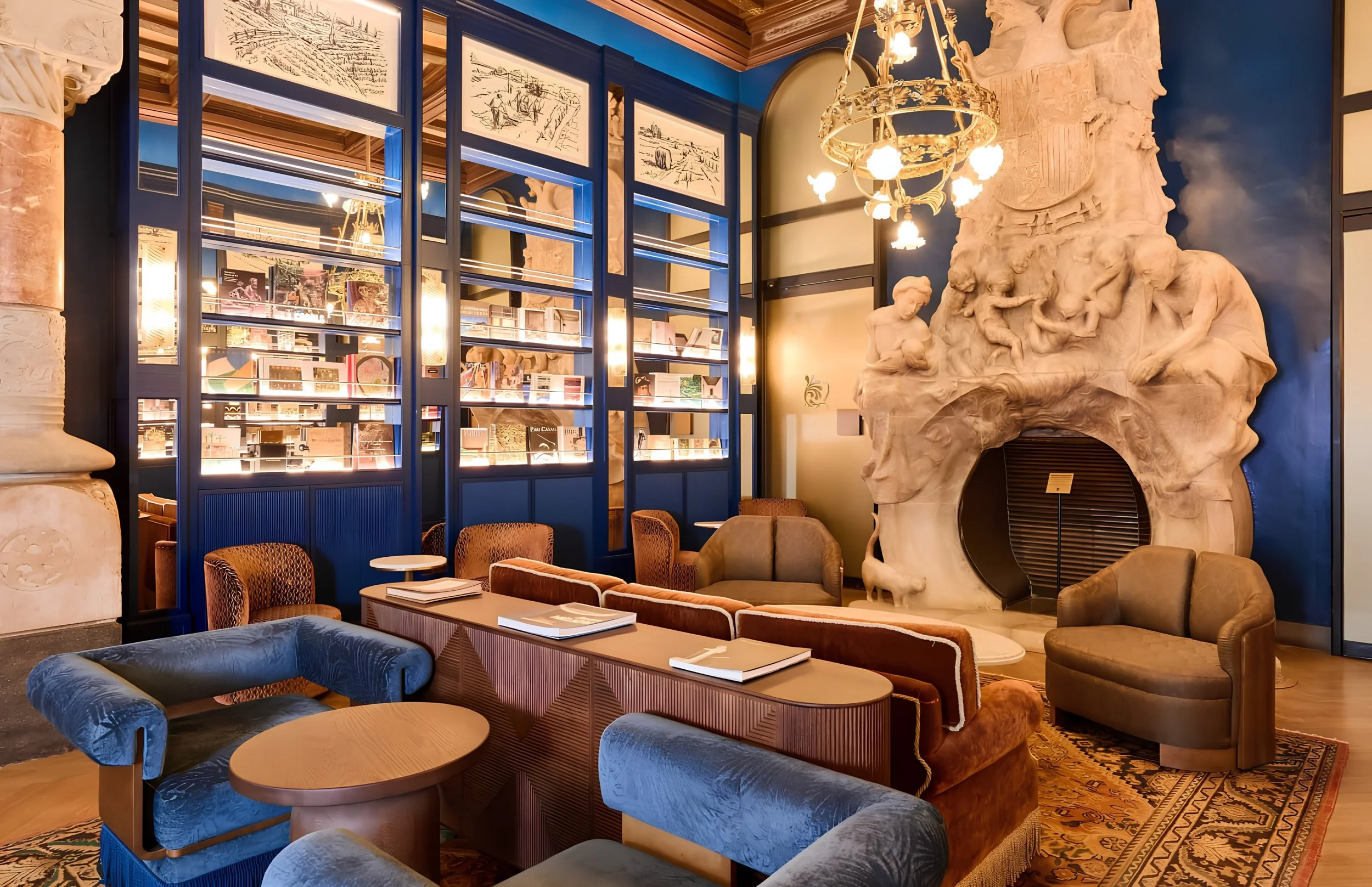 Interior of a stylish lounge or hotel lobby with blue and beige furniture, a large sculpture of a reclining figure, and decorative framed sketches on the wall.