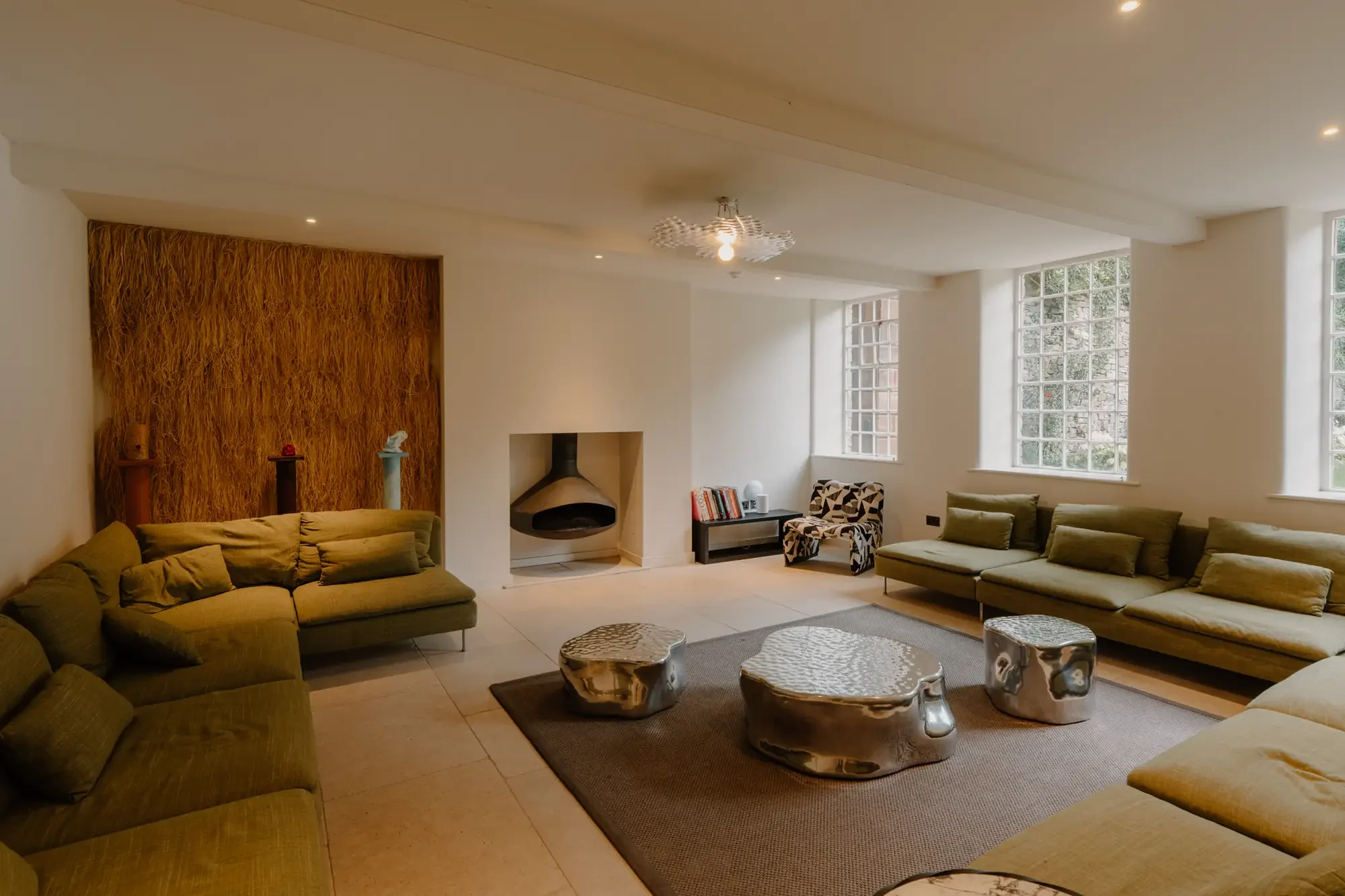 Living room with beige sofas, a textured accent wall, a fireplace, large windows, and modern silver stools