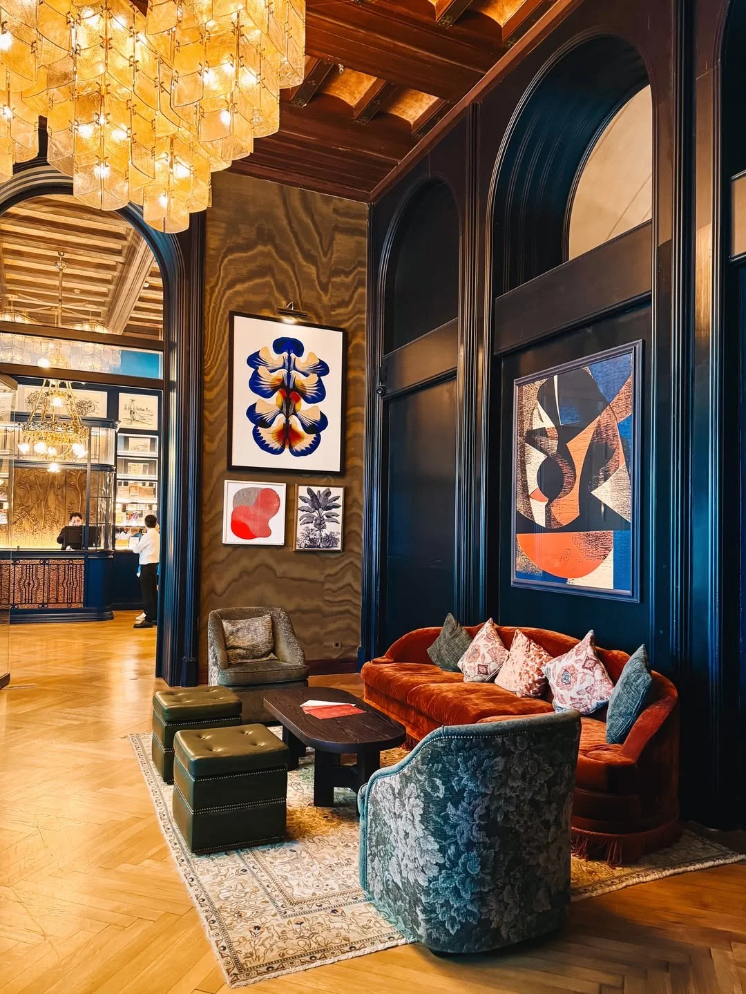 Elegant hotel lobby with a dark wood-paneled wall, modern abstract art, plush velvet seating, and a chandelier with gold accents.
