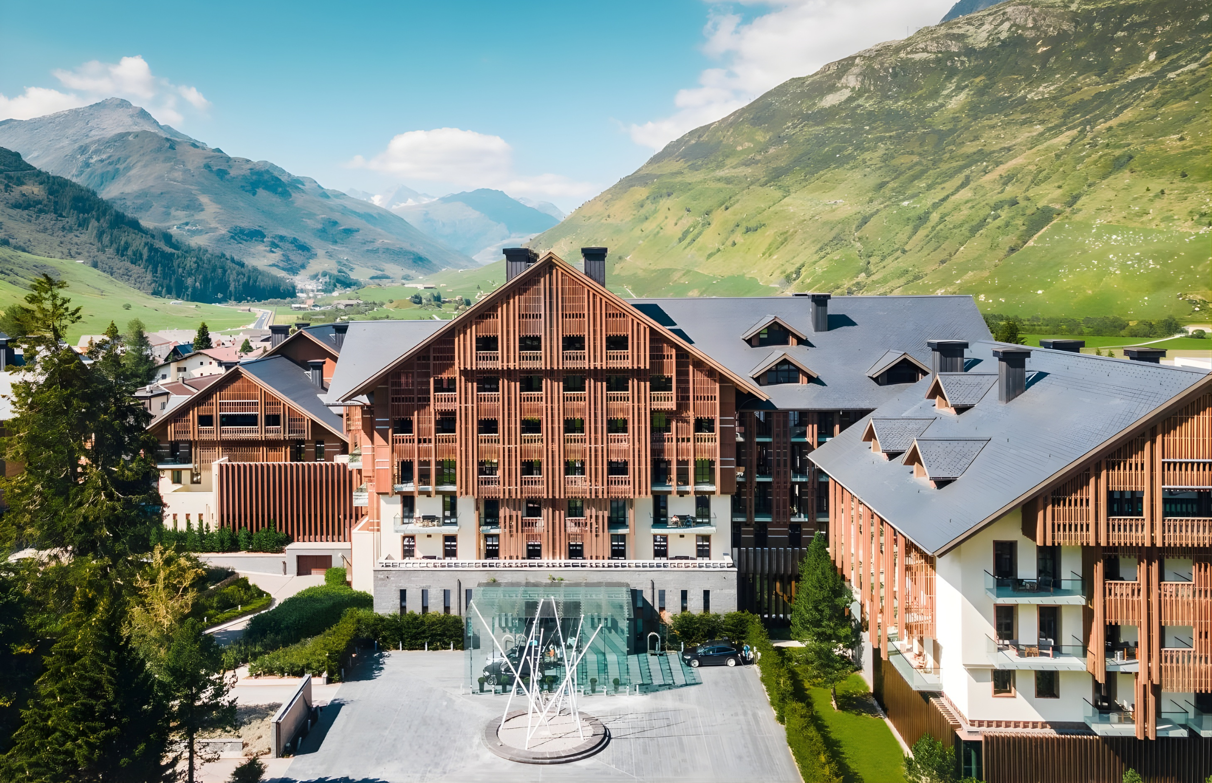 Modern residential buildings with a backdrop of green mountains and blue sky in a scenic mountain town.