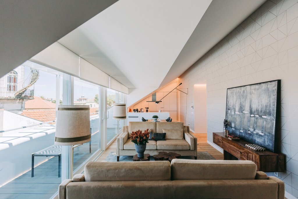 Modern living room with large windows, beige sofas, a wooden TV stand with a large painting, and a small balcony with outdoor furniture.
