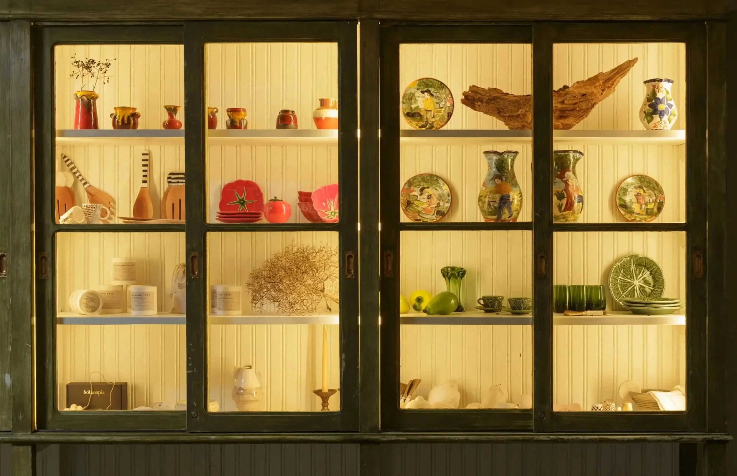 A black display cabinet with glass doors and yellow interior, showcasing various decorative ceramic vases, bowls, and plates with colorful patterns and designs.