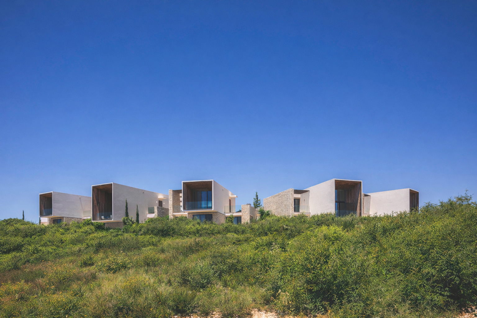 Modern residential houses on a green hillside under a clear blue sky.