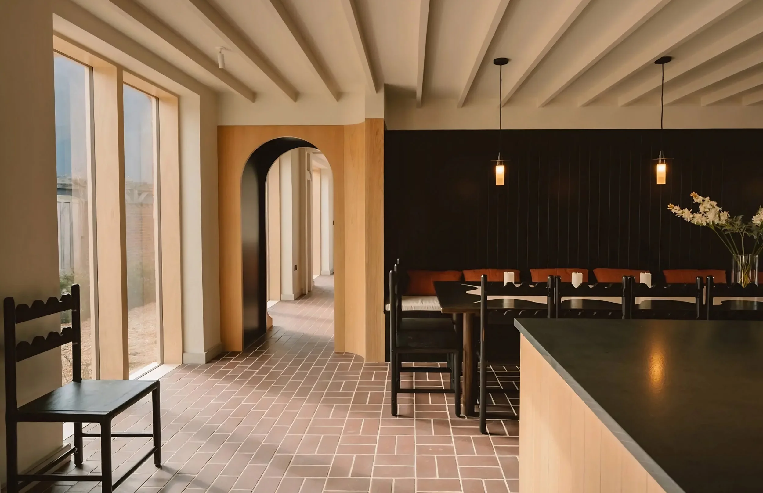 Interior of a modern dining area with black chairs, a black table, pendant lights, a floral arrangement, large windows, and wood and black wall accents.