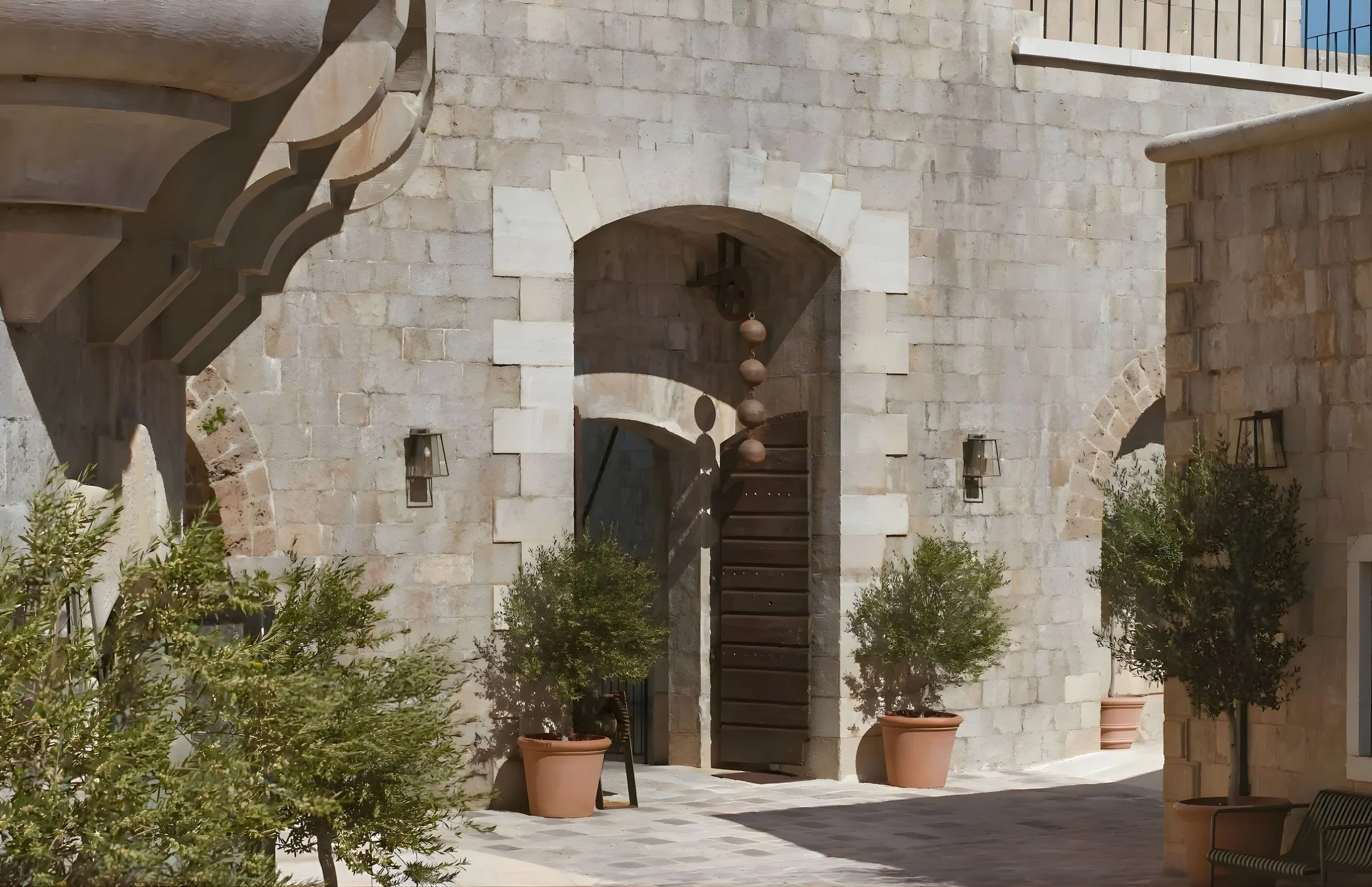 Sunny courtyard with stone archway, staircase, potted plants, and outdoor seating.