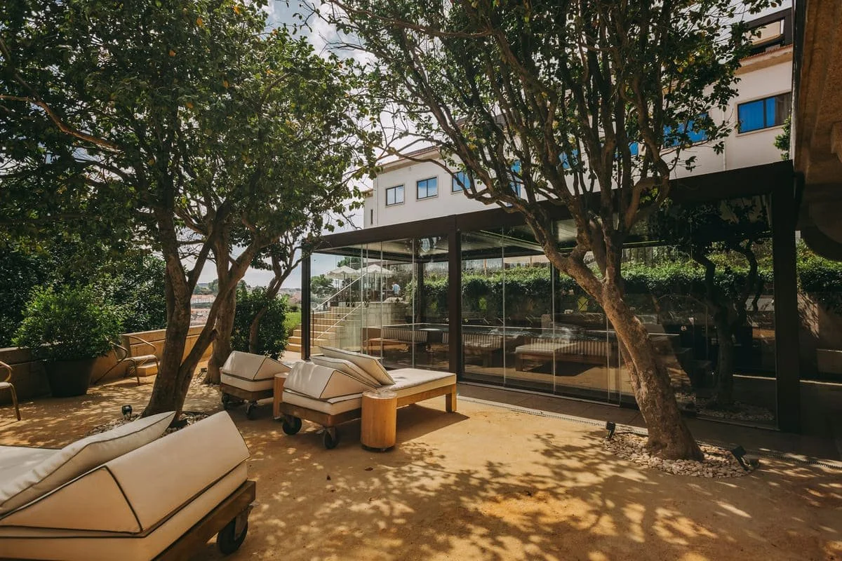 Outdoor patio with beige lounge chairs, trees, and a modern glass building in the background.