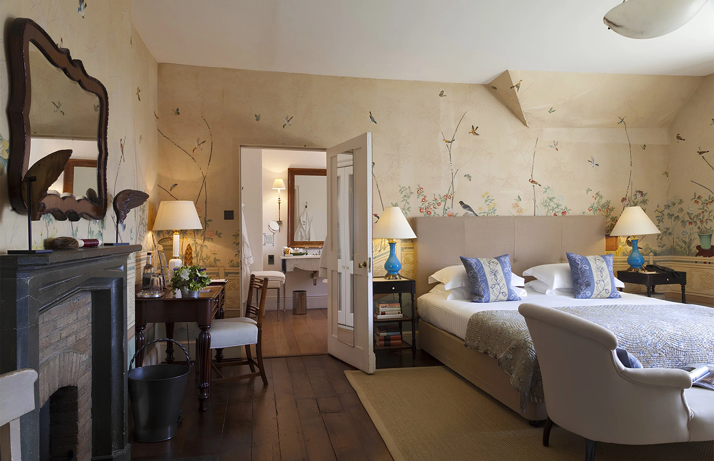 A cozy bedroom with a large bed, pillows, table lamps, and decorative wallpaper featuring birds and floral design.