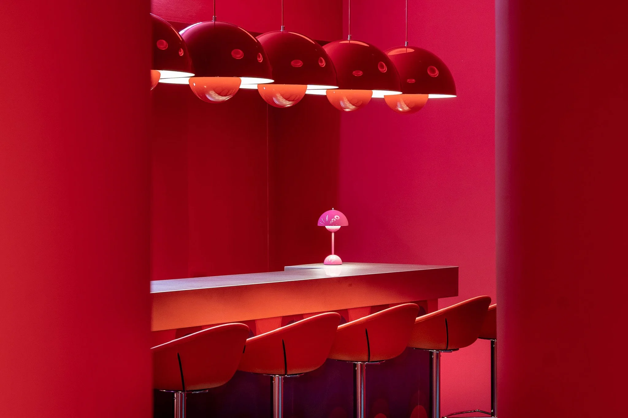 Modern red and pink pendant lights hanging above a red counter with red chairs against a red wall.