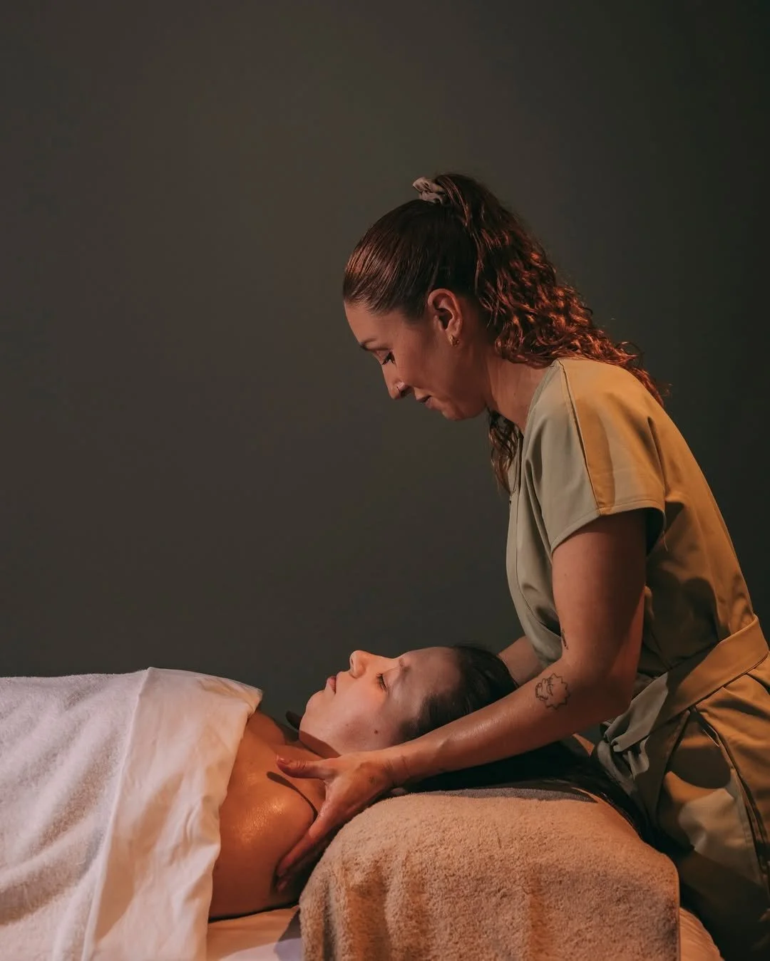 A massage therapist giving a massage to a woman lying face up on a massage table.
