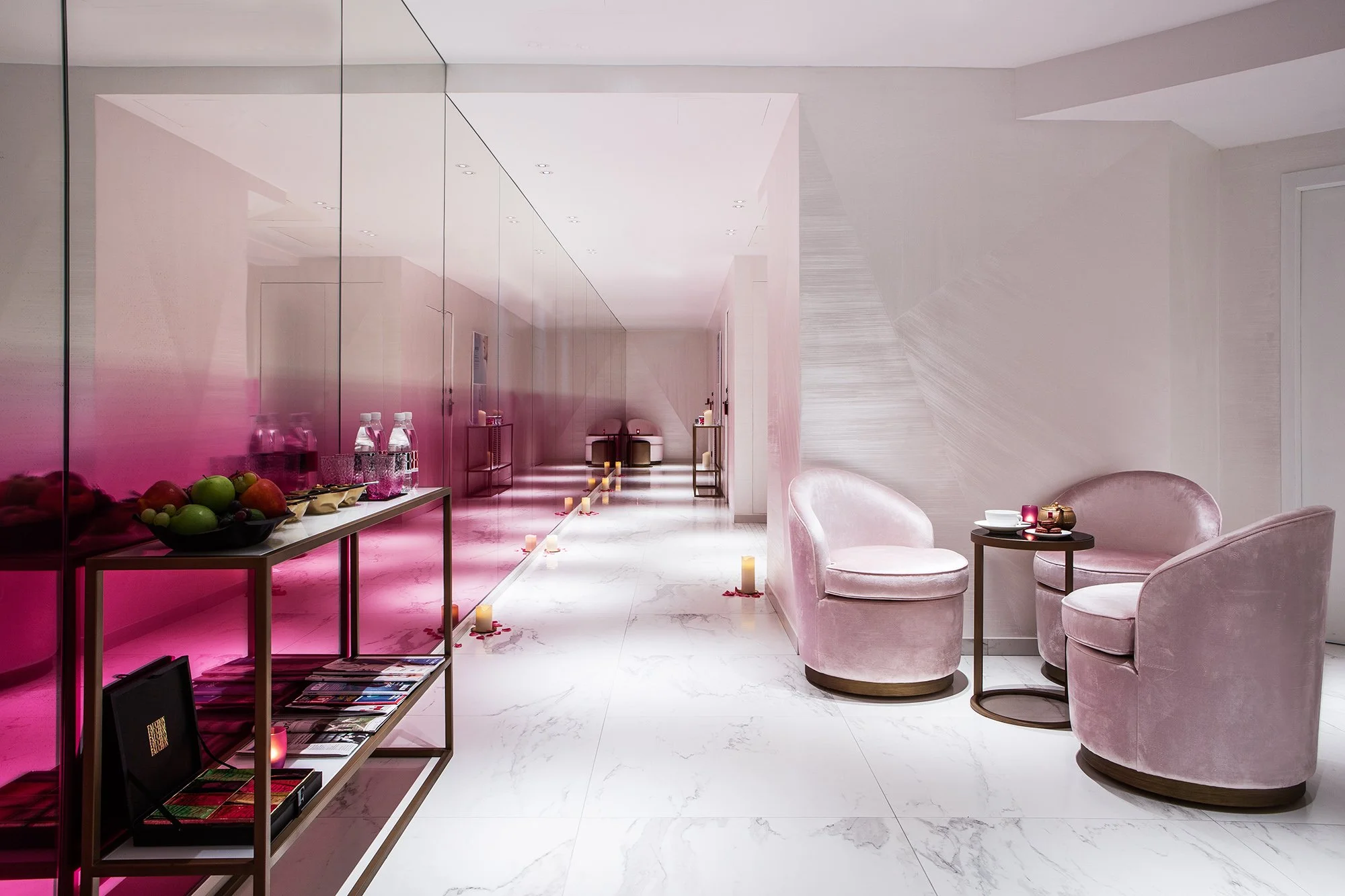 Modern interior room with pink velvet armchairs, a side table, and a row of candles on the floor, decorated for a romantic occasion.
