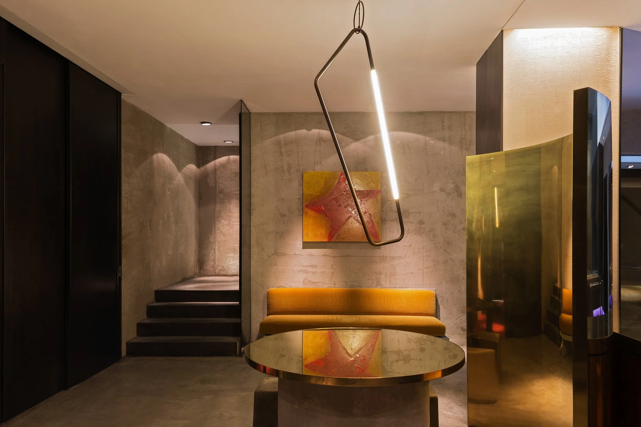 Modern hotel lobby with a yellow velvet sofa, a round coffee table, abstract artwork on the wall, and contemporary pendant lighting.
