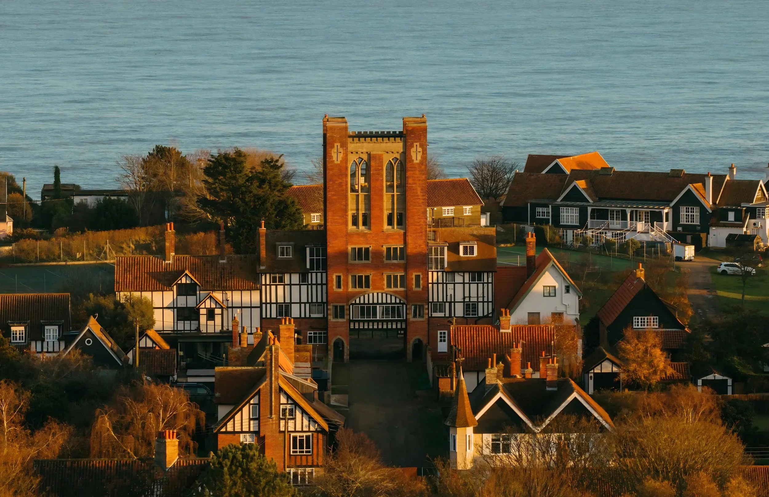 A coastal town with houses and a church with a distinctive twin-tower front façade, overlooking the sea at sunset.
