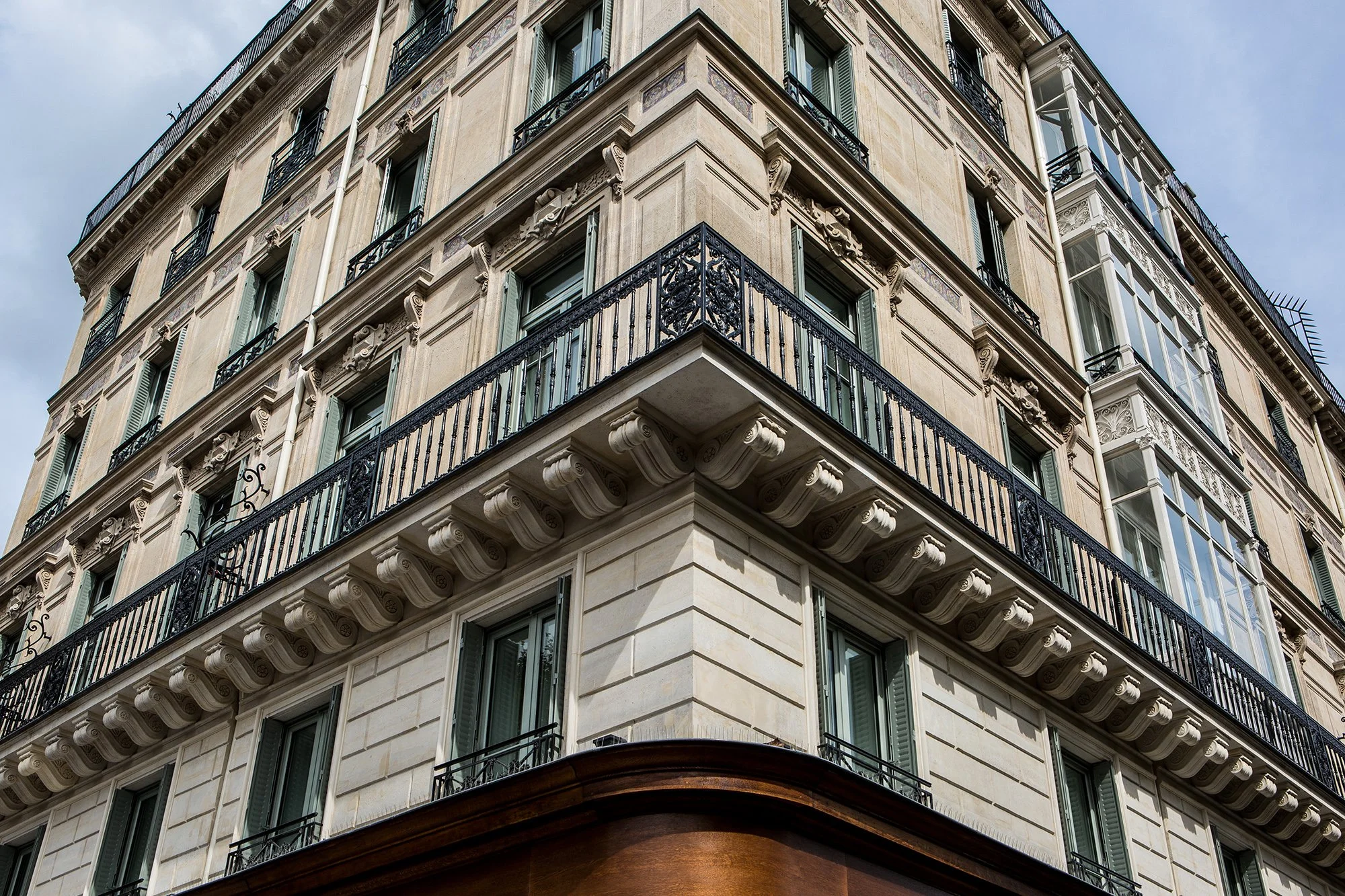 Exterior view of a historic multi-story building with ornate details, wrought iron balconies, and large windows, set against a cloudy sky.