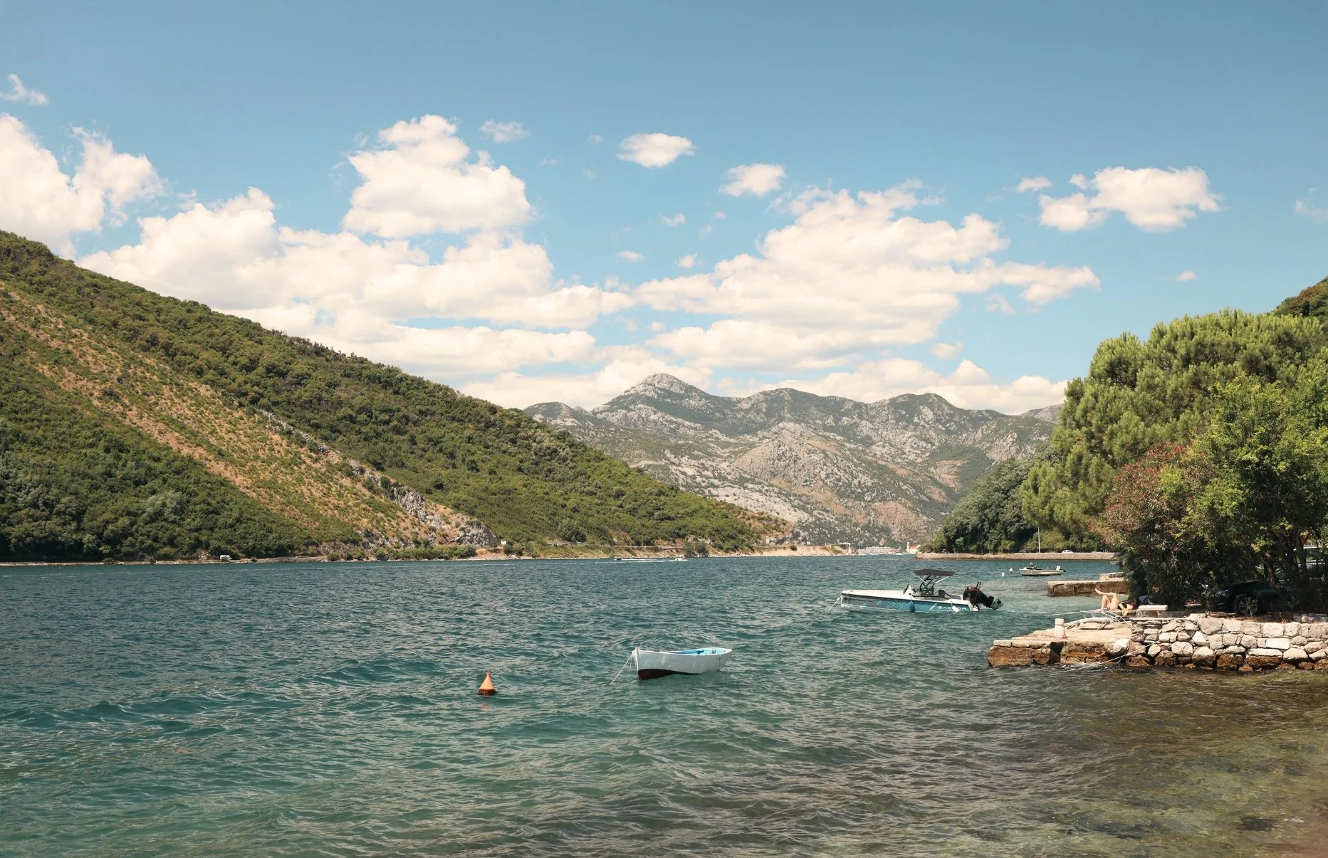 A scenic view of a lake with small boats floating on the water, surrounded by green mountains and a partly cloudy sky.