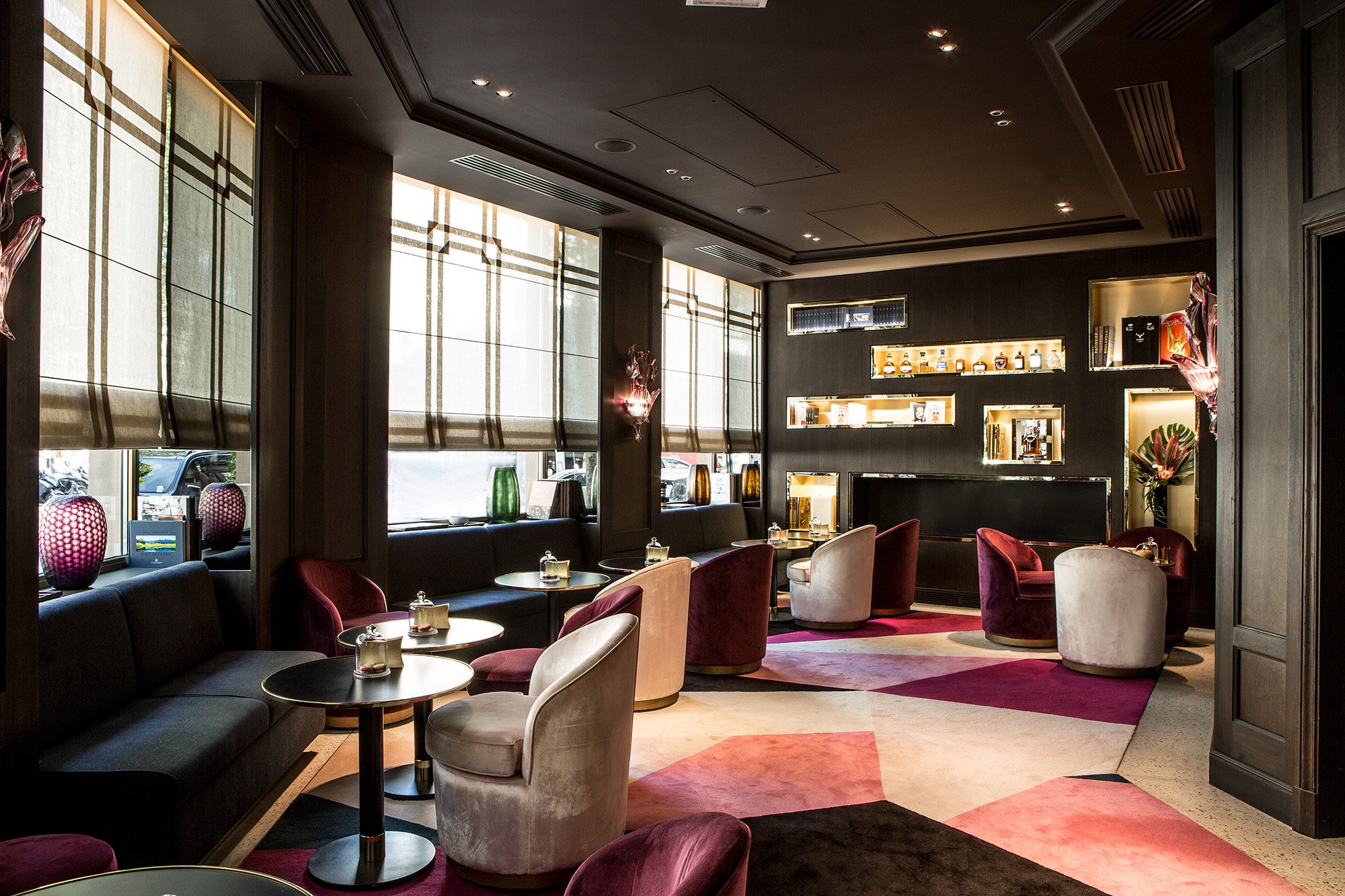 Interior of a modern lounge or restaurant with large windows, plush chairs, and decorative lighting, featuring a dark color scheme with black walls and ceiling.