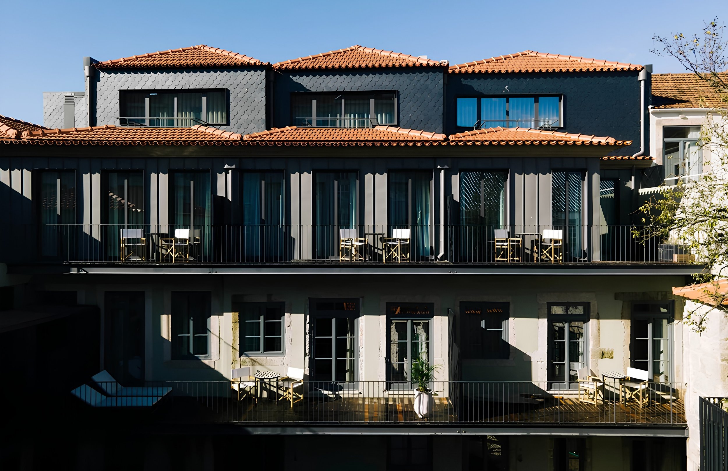 A multi-story residential building with glass balcony doors, red tiled roofs, and black and white exterior walls, under a clear blue sky.
