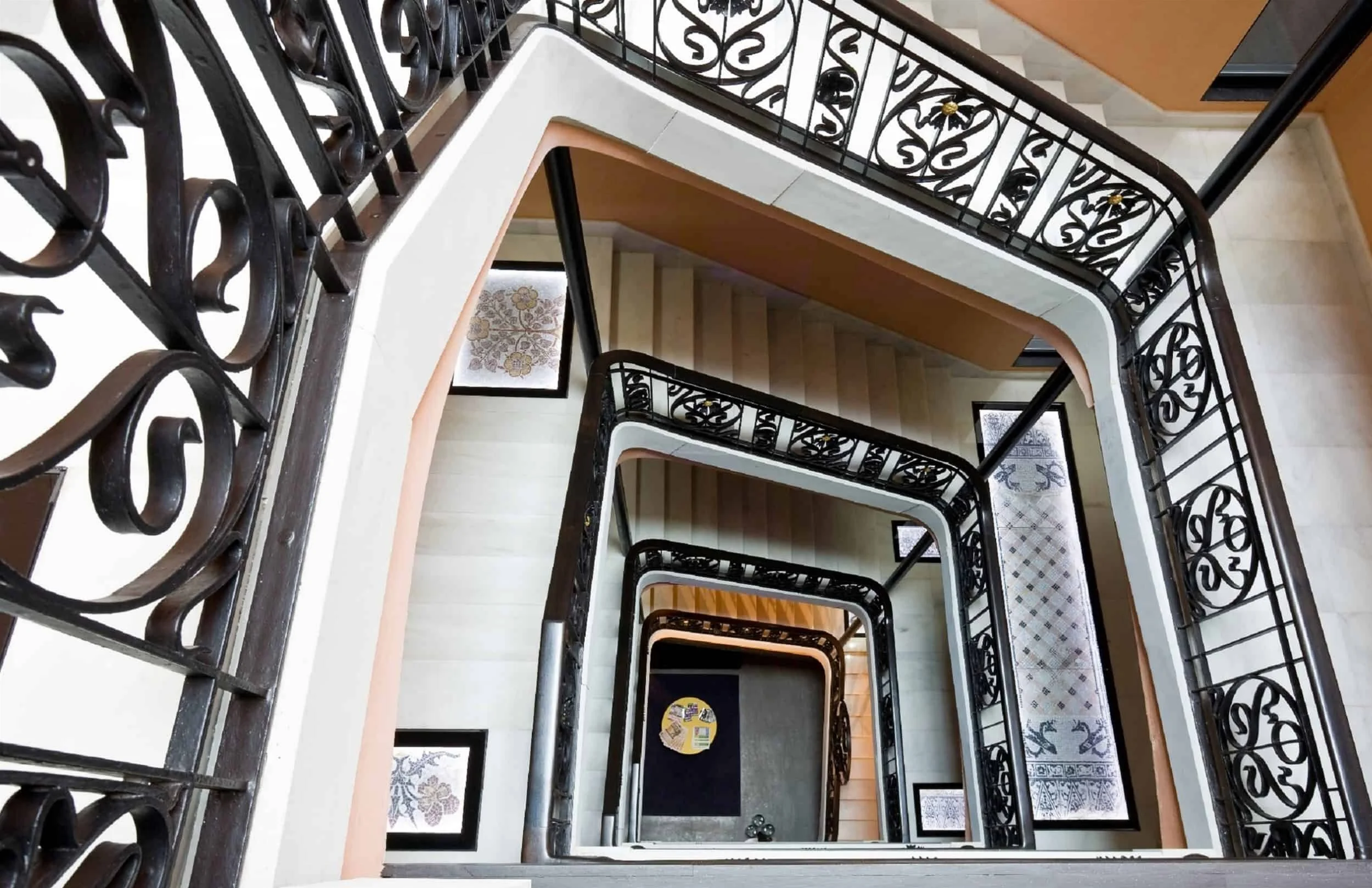 A view looking down the interior staircase with decorative black wrought iron railings and patterned tile flooring.