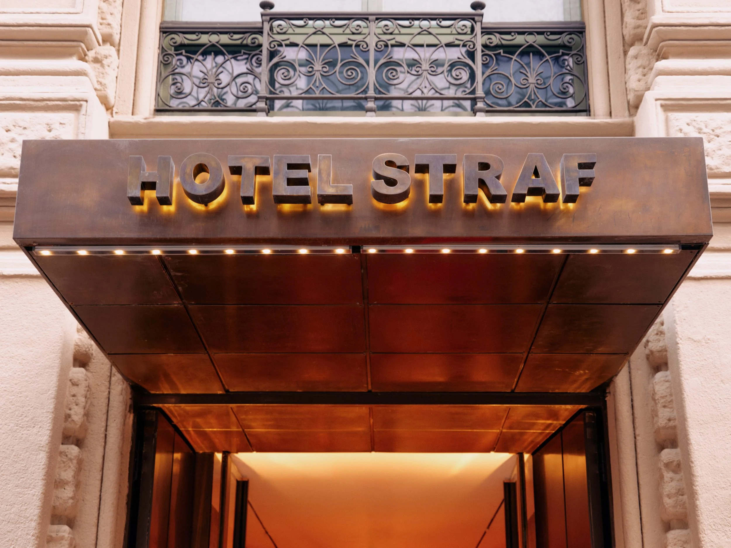 Hotel Strasbourg sign with stone and wrought iron balcony above, entrance with warm lighting, in an elegant building.