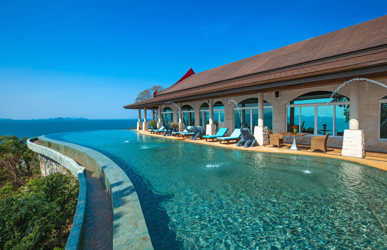Luxury hotel with an infinity pool overlooking the ocean, with sculptures of frogs on the poolside, blue sky, and clear weather.