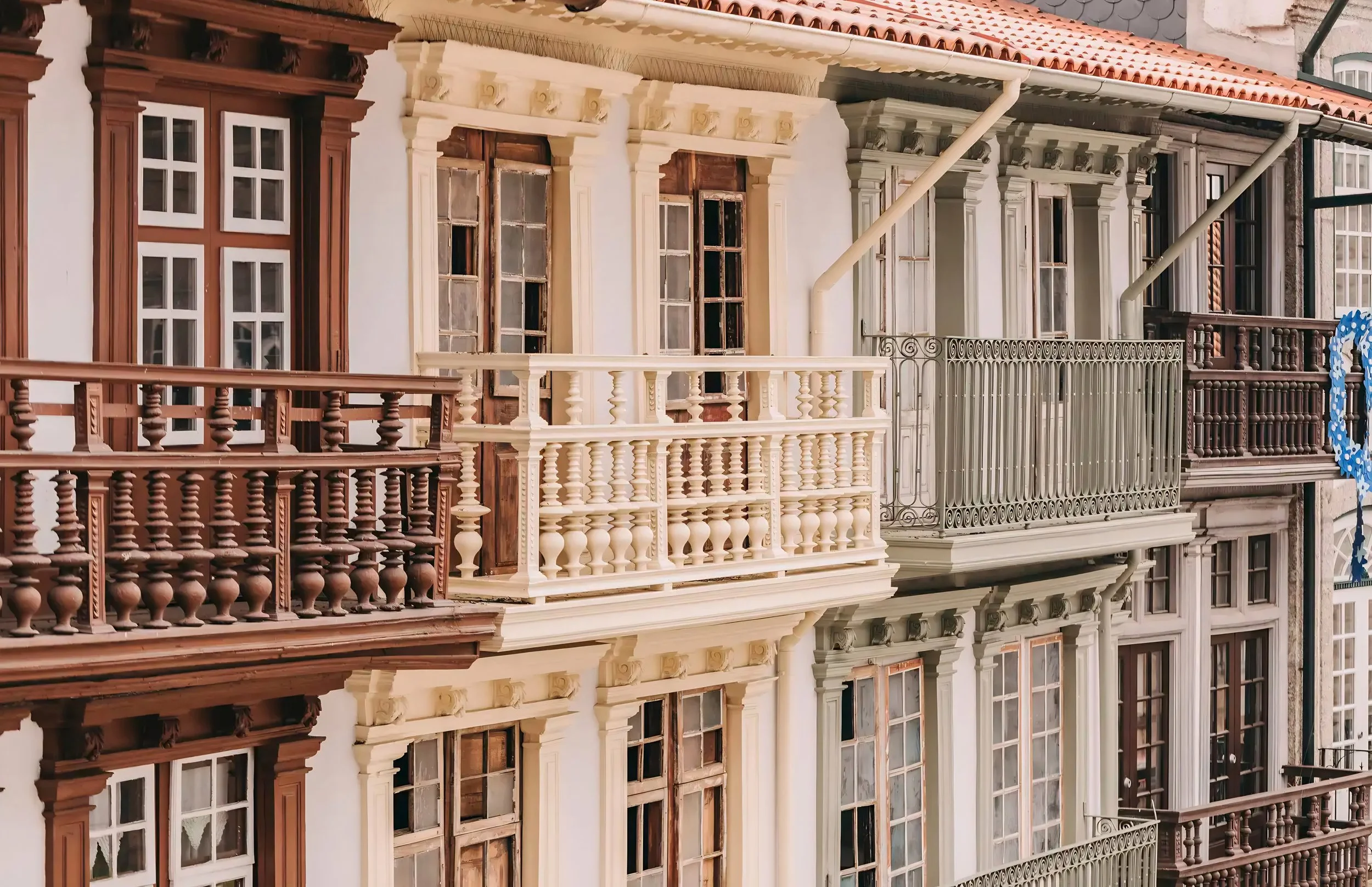 Multiple historical buildings with ornate birdcage-style balconies and old wooden framed windows on a city street.