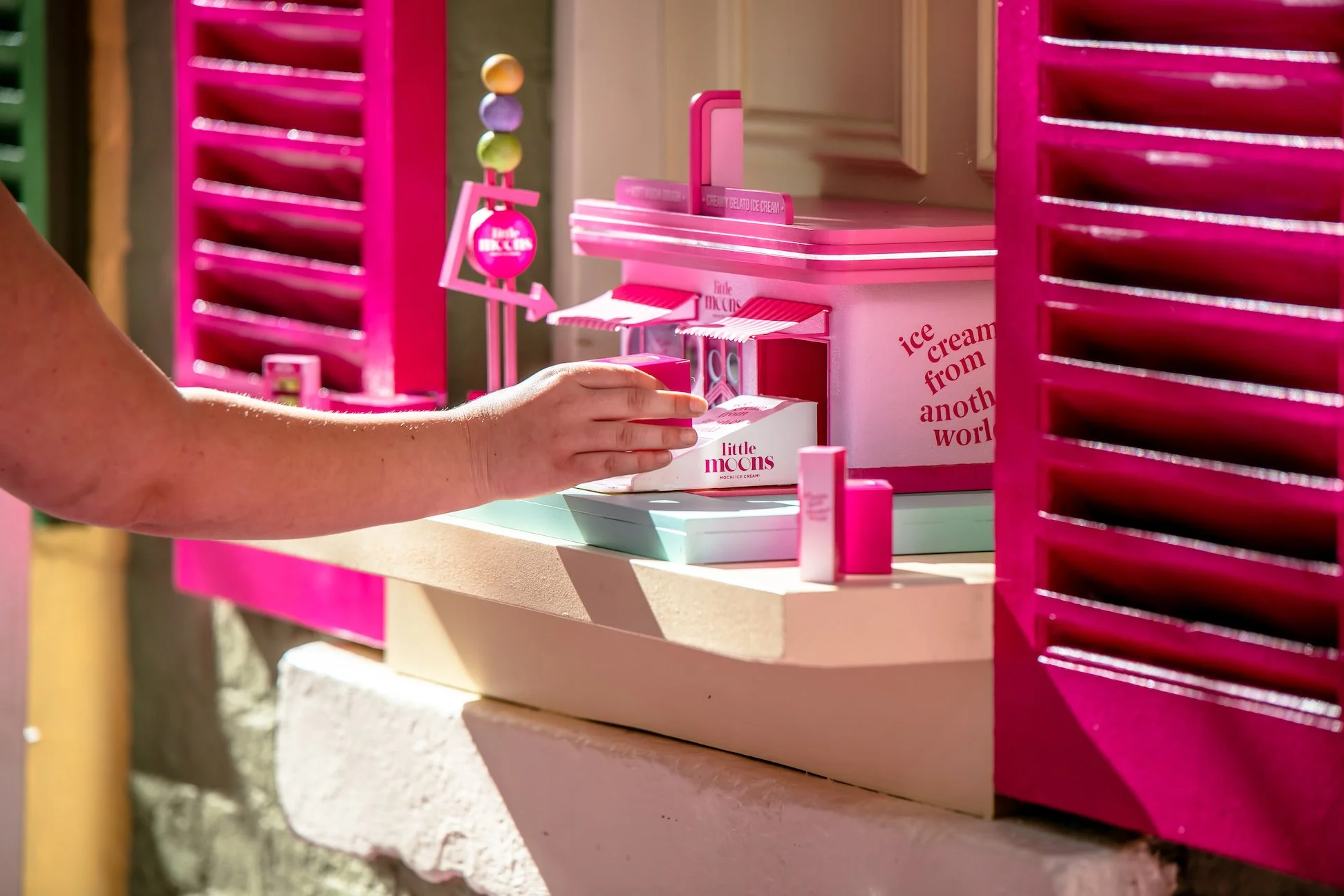 Child's hand reaching into a pink ice cream truck playset with miniature ice cream boxes and accessories.