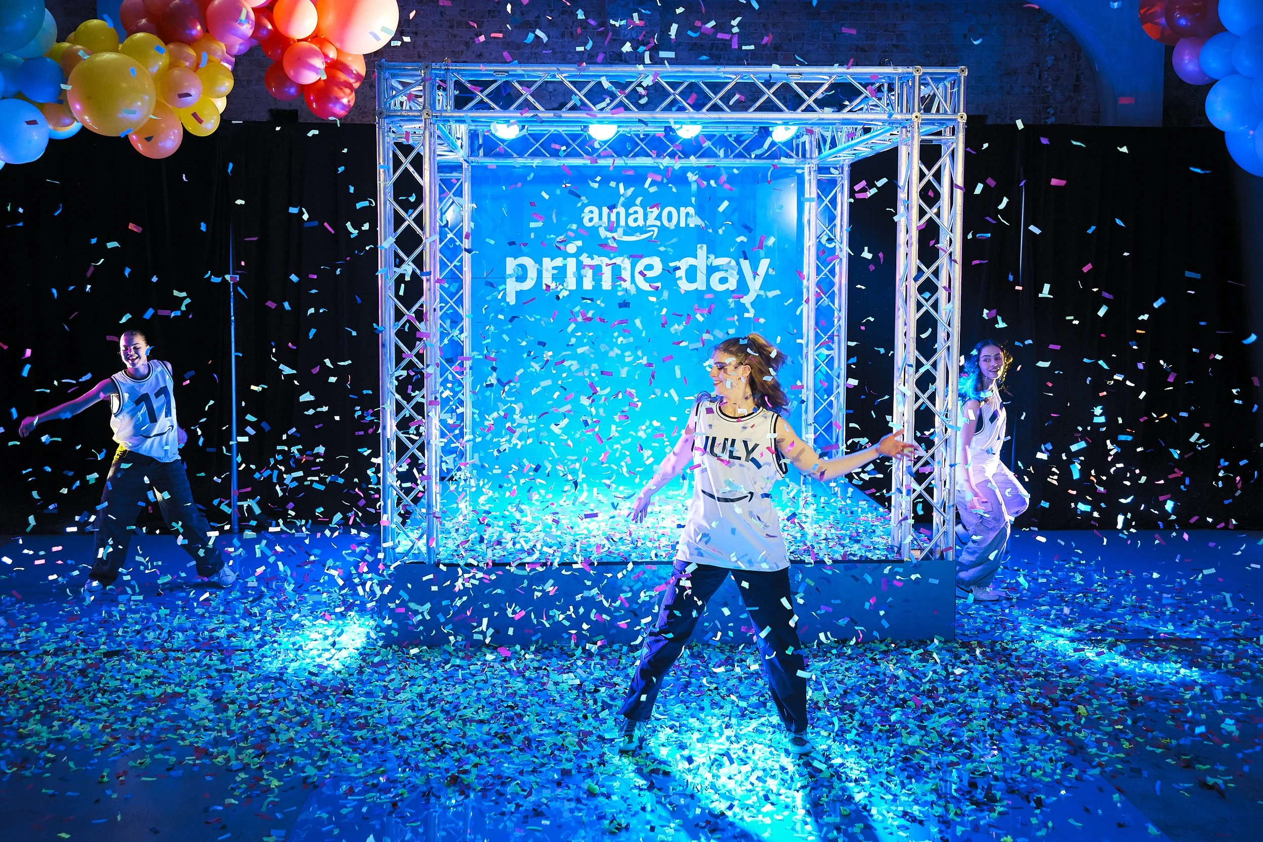 People celebrating Amazon Prime Day with confetti and balloons, stage with 'Amazon Prime Day' text.