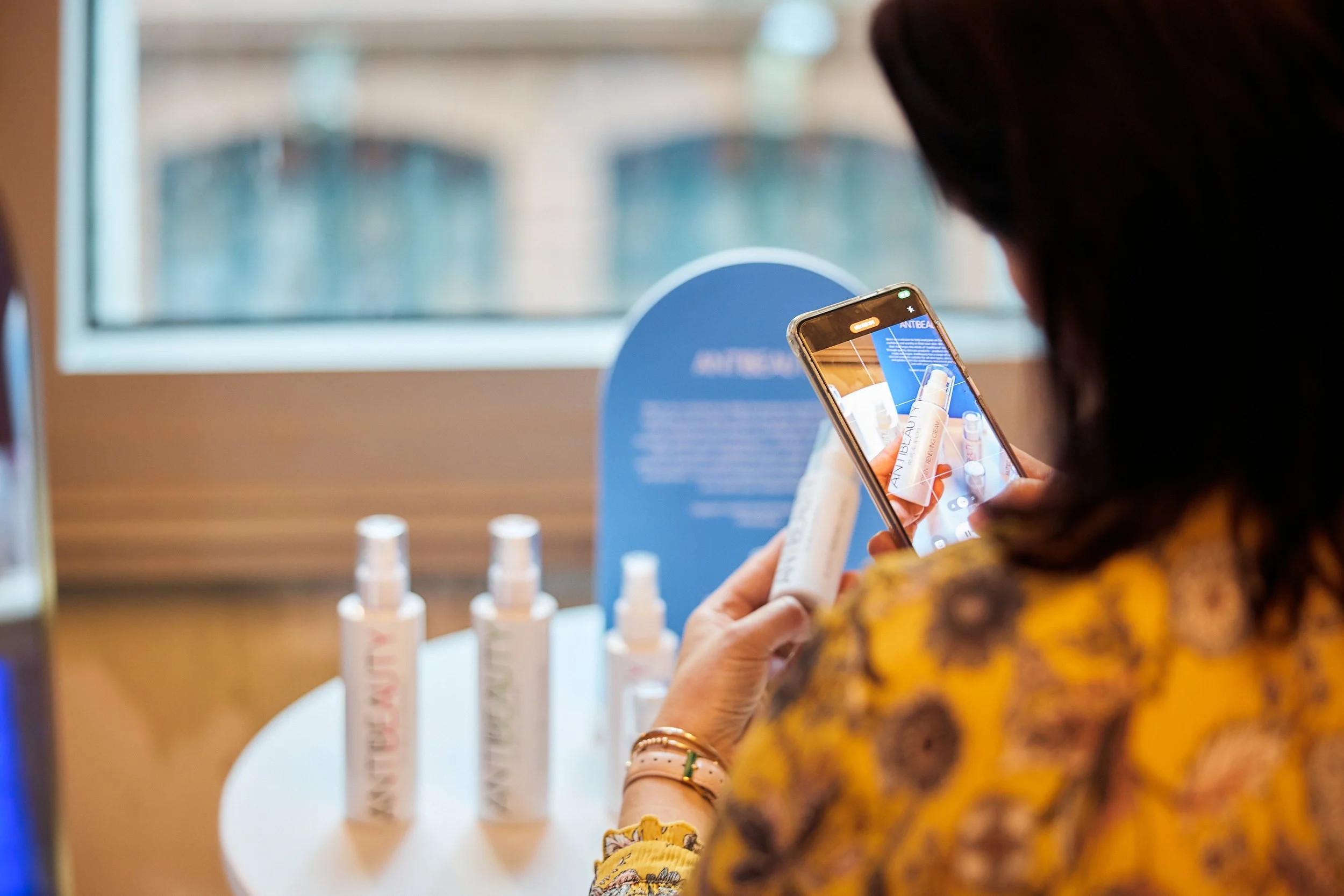 Person taking a photo of skincare products on display with a smartphone.