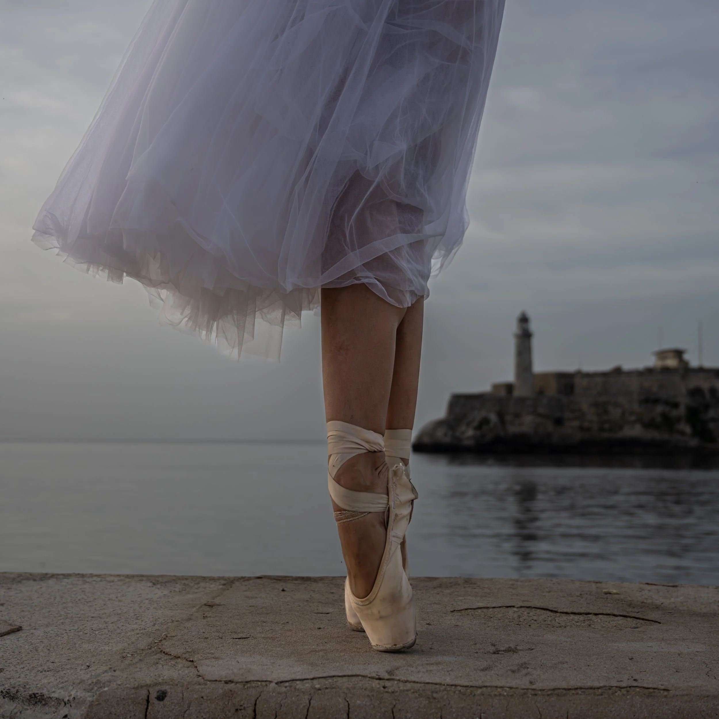 Ballerina standing on pointe by El Morro fortress in Habana, Cuba at dusk, fine art photography by Liza Camilo