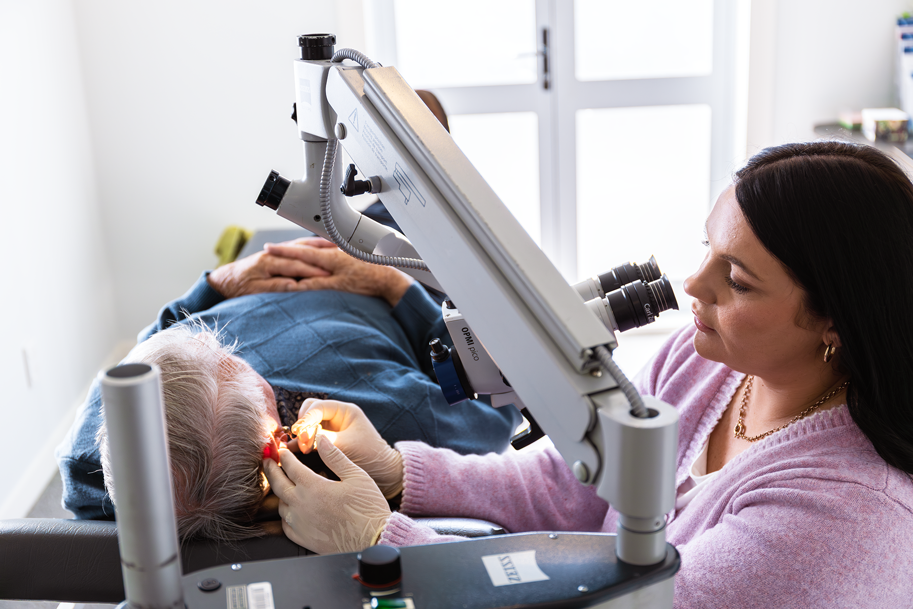 A female dentist examines an elderly patient using a microscope in a dental clinic.