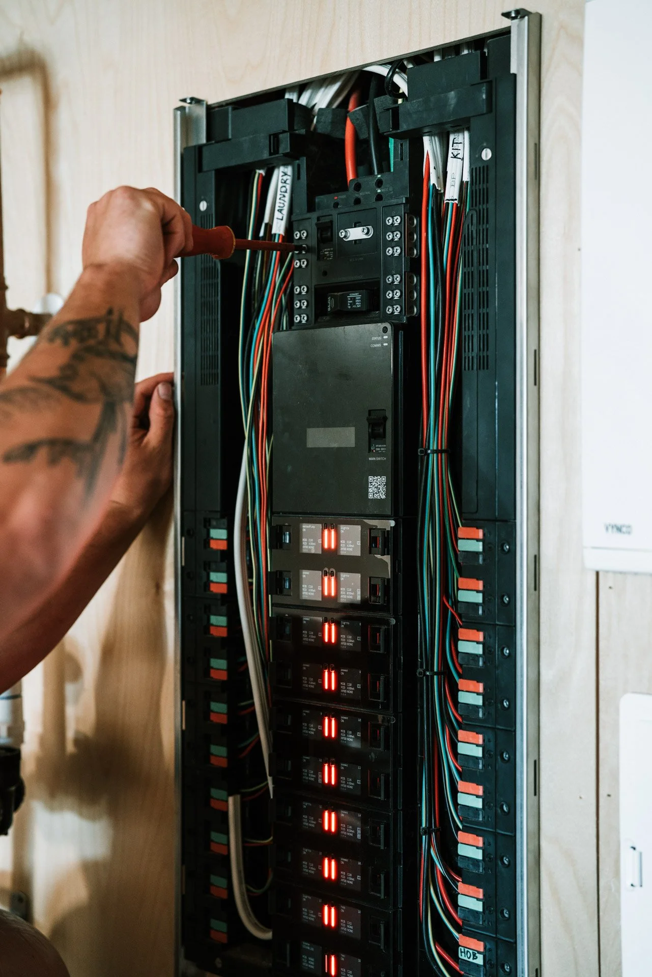 A person working on an electrical panel or circuit breaker box mounted on a wooden wall, using a screwdriver.