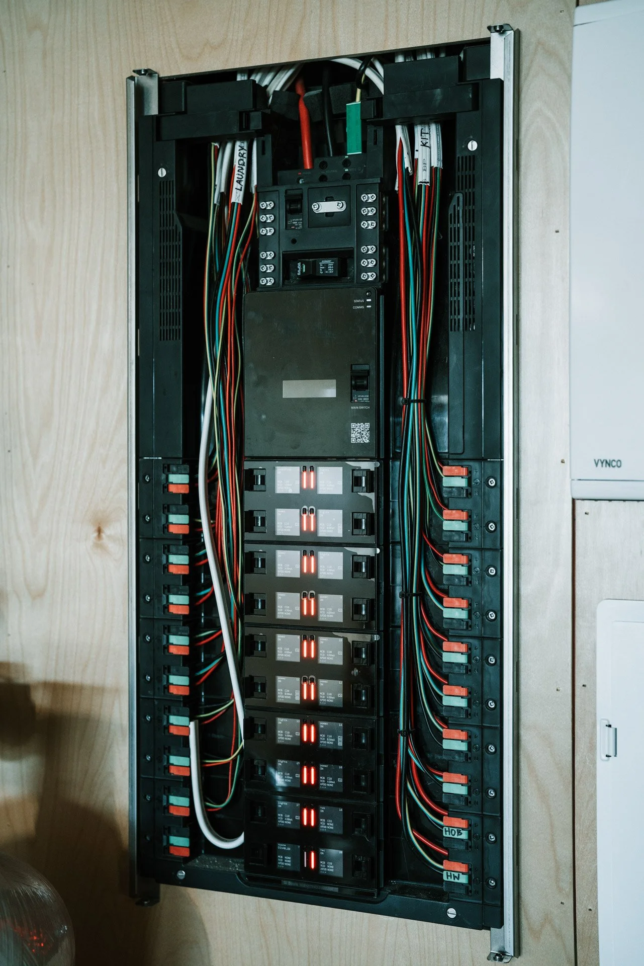 Electrical panel with organized wires and circuit breakers mounted on a wooden wall.