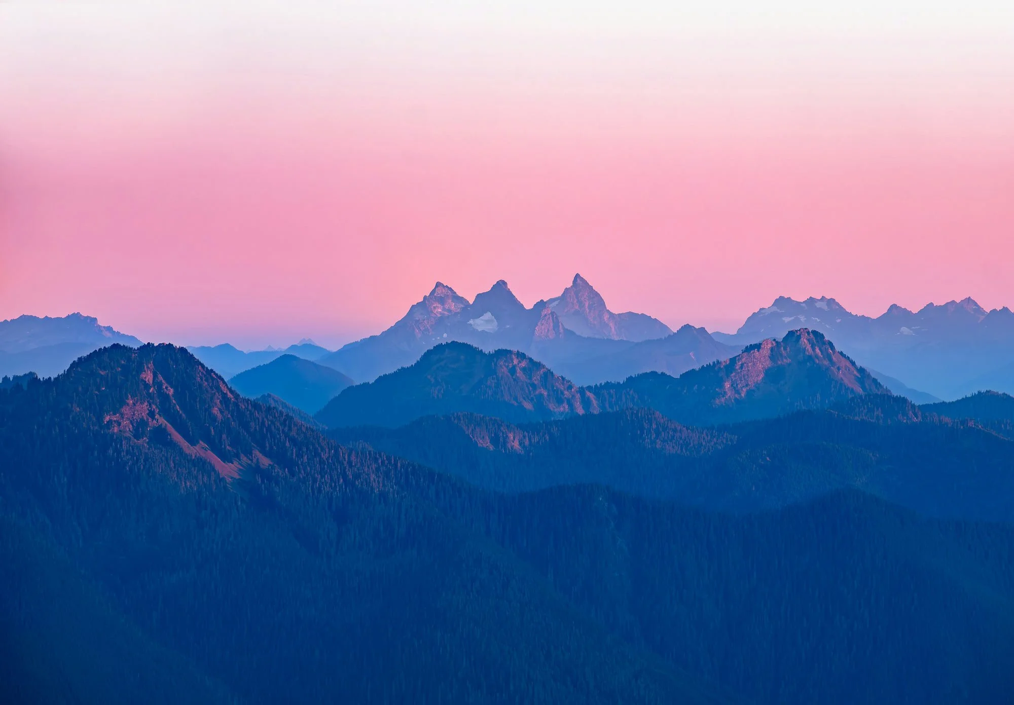 A mountain landscape at sunset with layered mountain ridges and a pink sky.