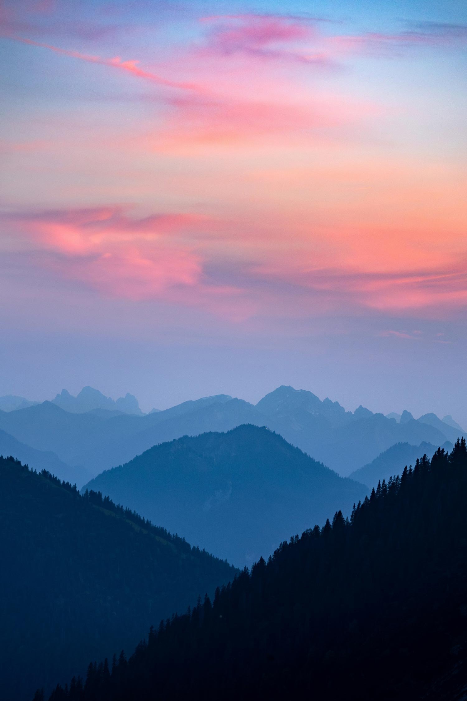 A mountain range viewed at dusk with pink and purple clouds in the sky.