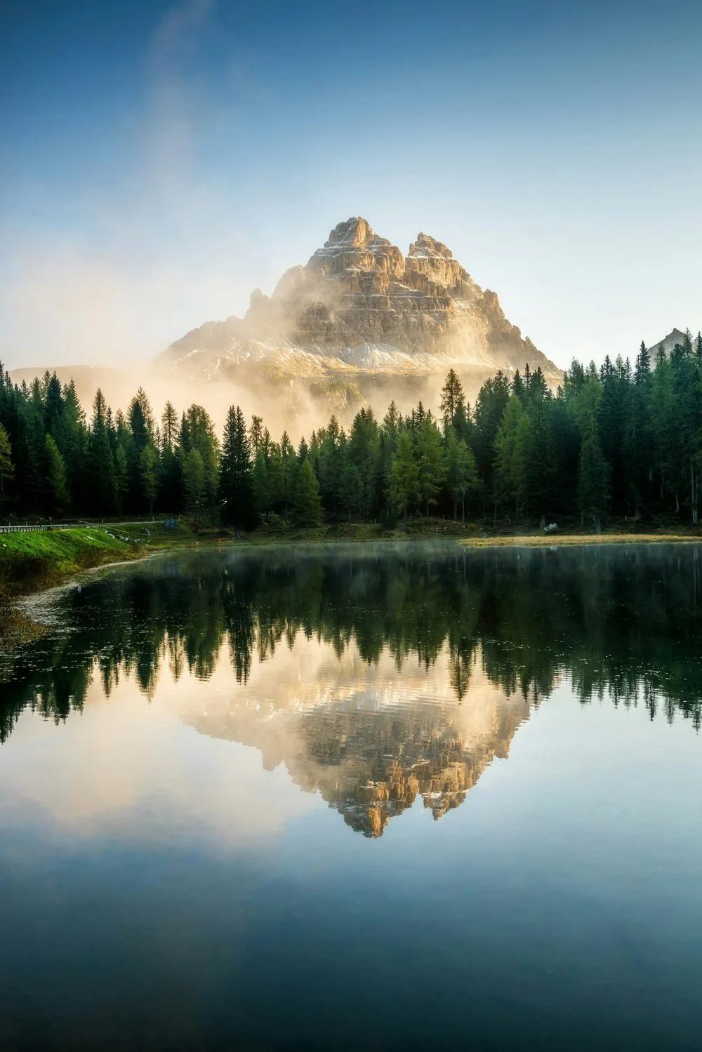 Majestic mountain behind a dense green forest and a calm lake reflecting the mountain and forest in the foreground.