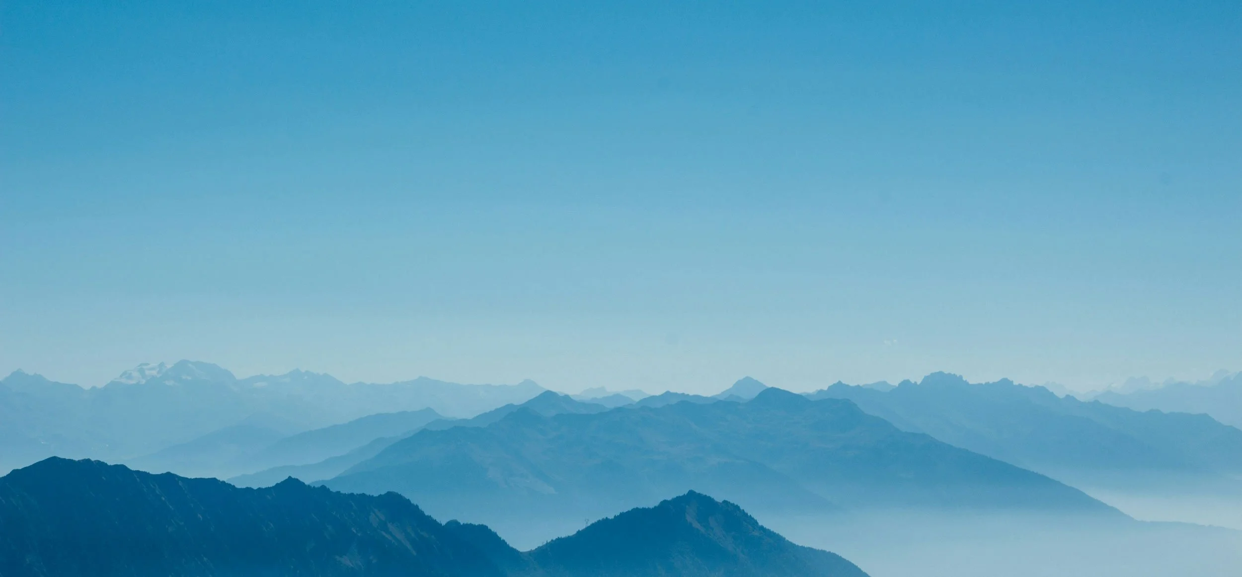 A vast mountain range with multiple layers of mountains fading into the distance under a clear blue sky.