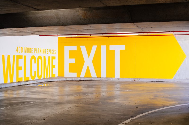 Large yellow and white sign in an underground parking garage indicating 'WELCOME EXIT' with an arrow pointing to the right, and a note about 400 more parking spaces.