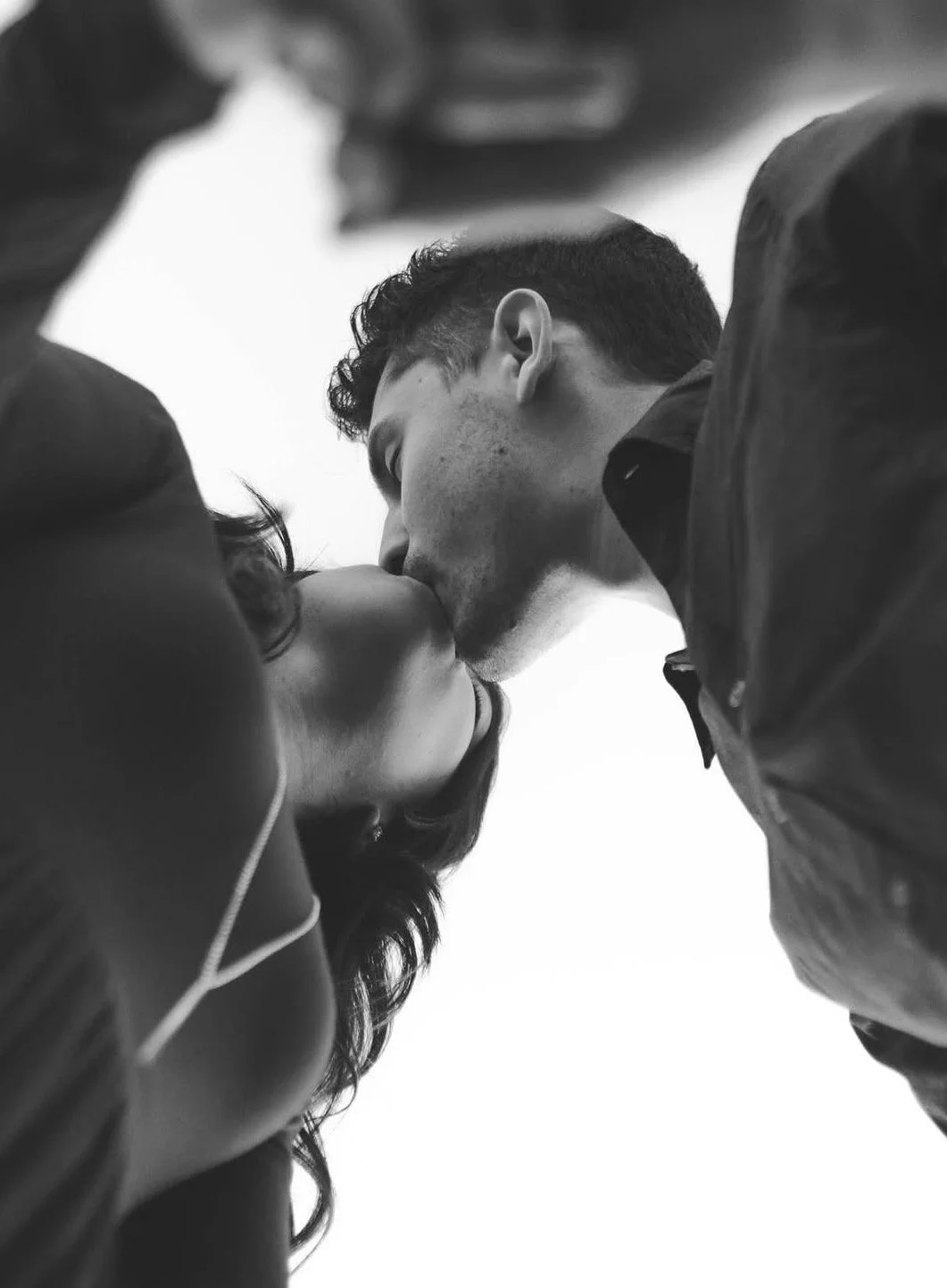 A black-and-white photo of a man and woman sharing a kiss from a low angle, with their faces close together.