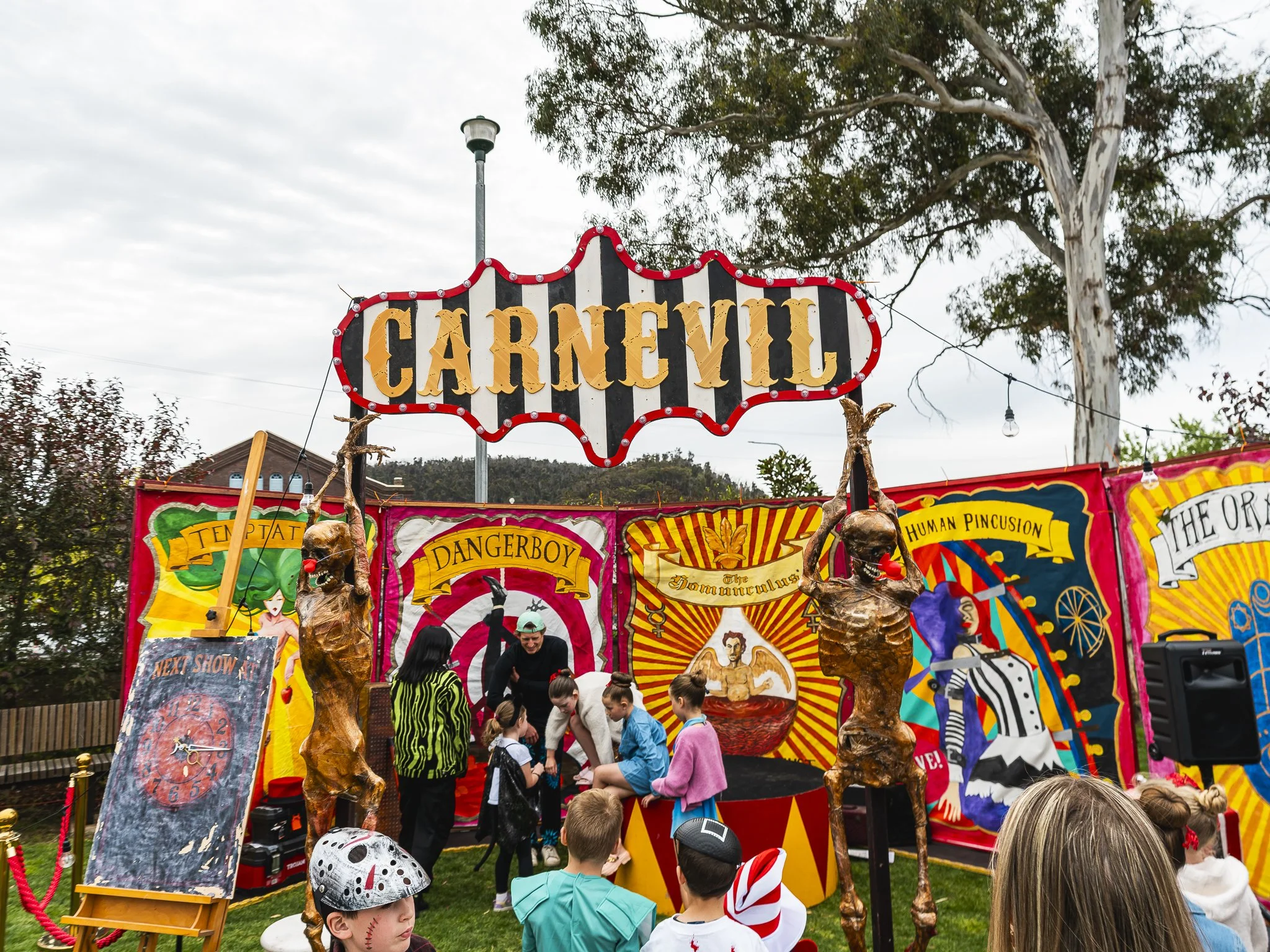 Carnival tent with colorful costumes, performers, and children watching a show.