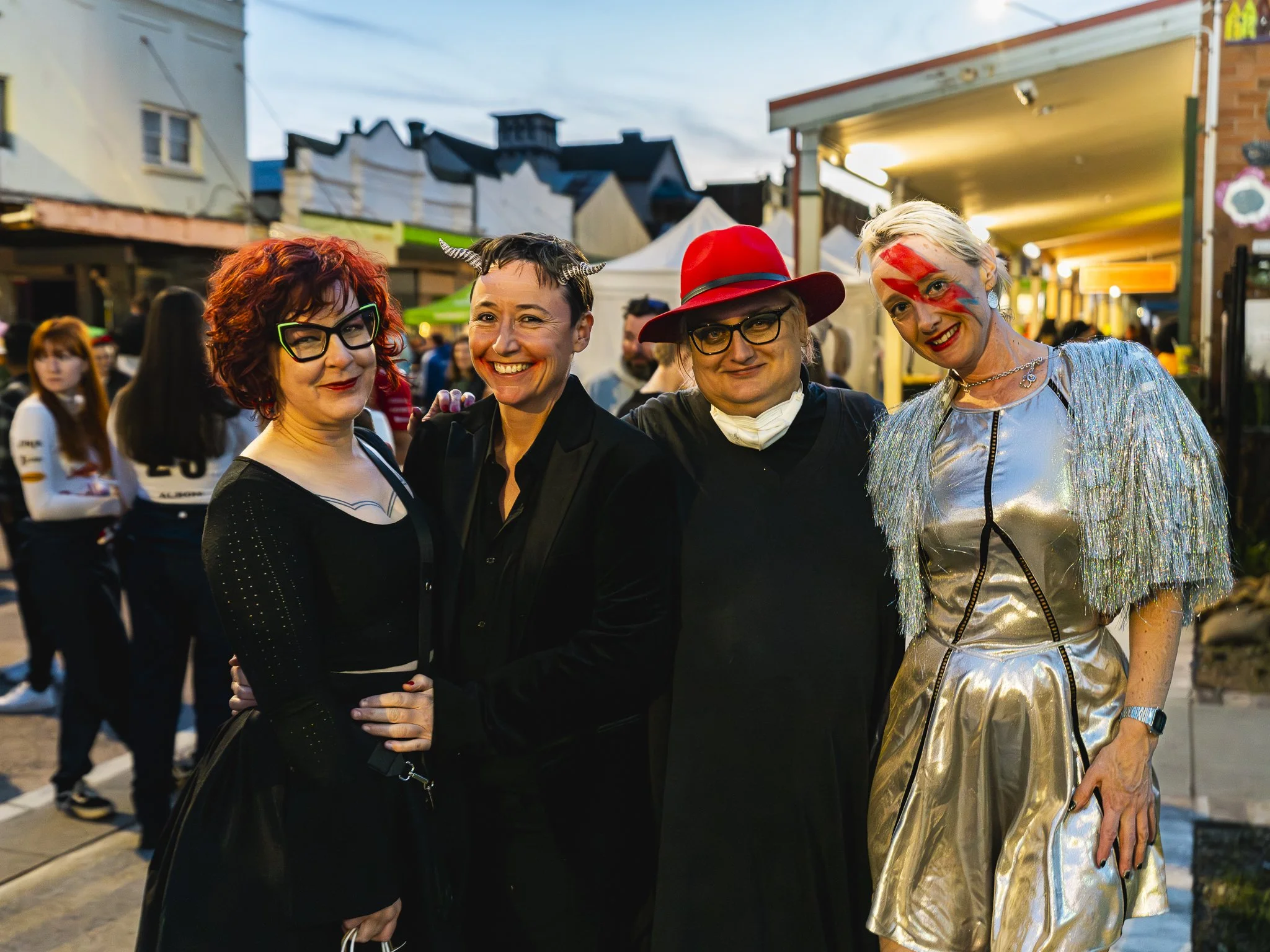 Four people dressed in costumes smile together at an outdoor event during the evening.