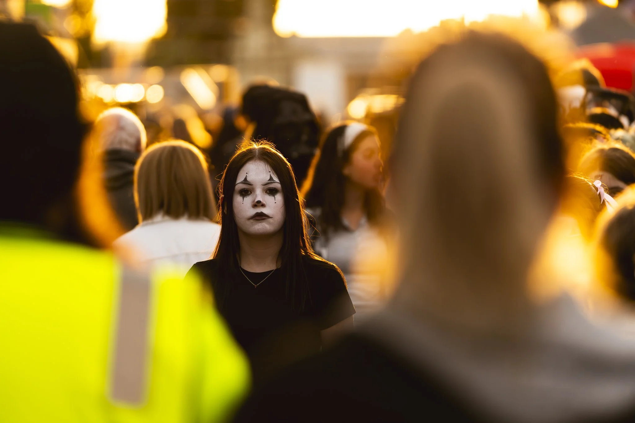 A young woman with dark makeup and black hair standing among a crowd at sunset.