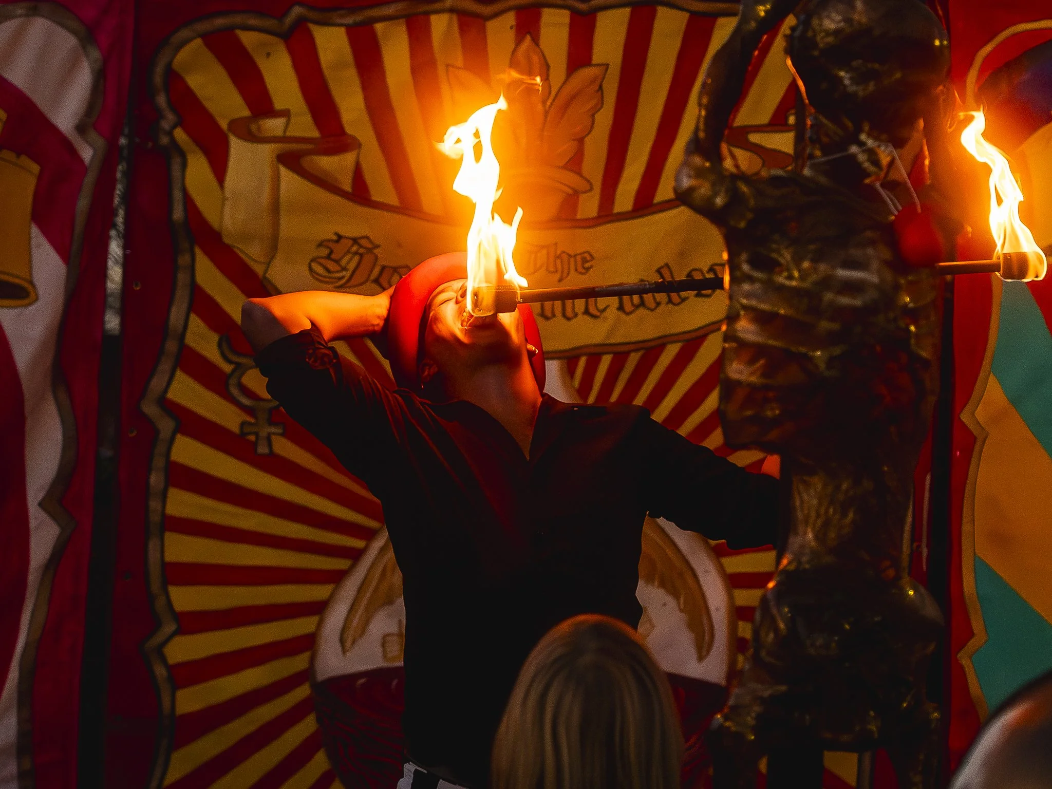 Performer dressed as a clown with a fire-eating act, with a colorful circus-themed backdrop.