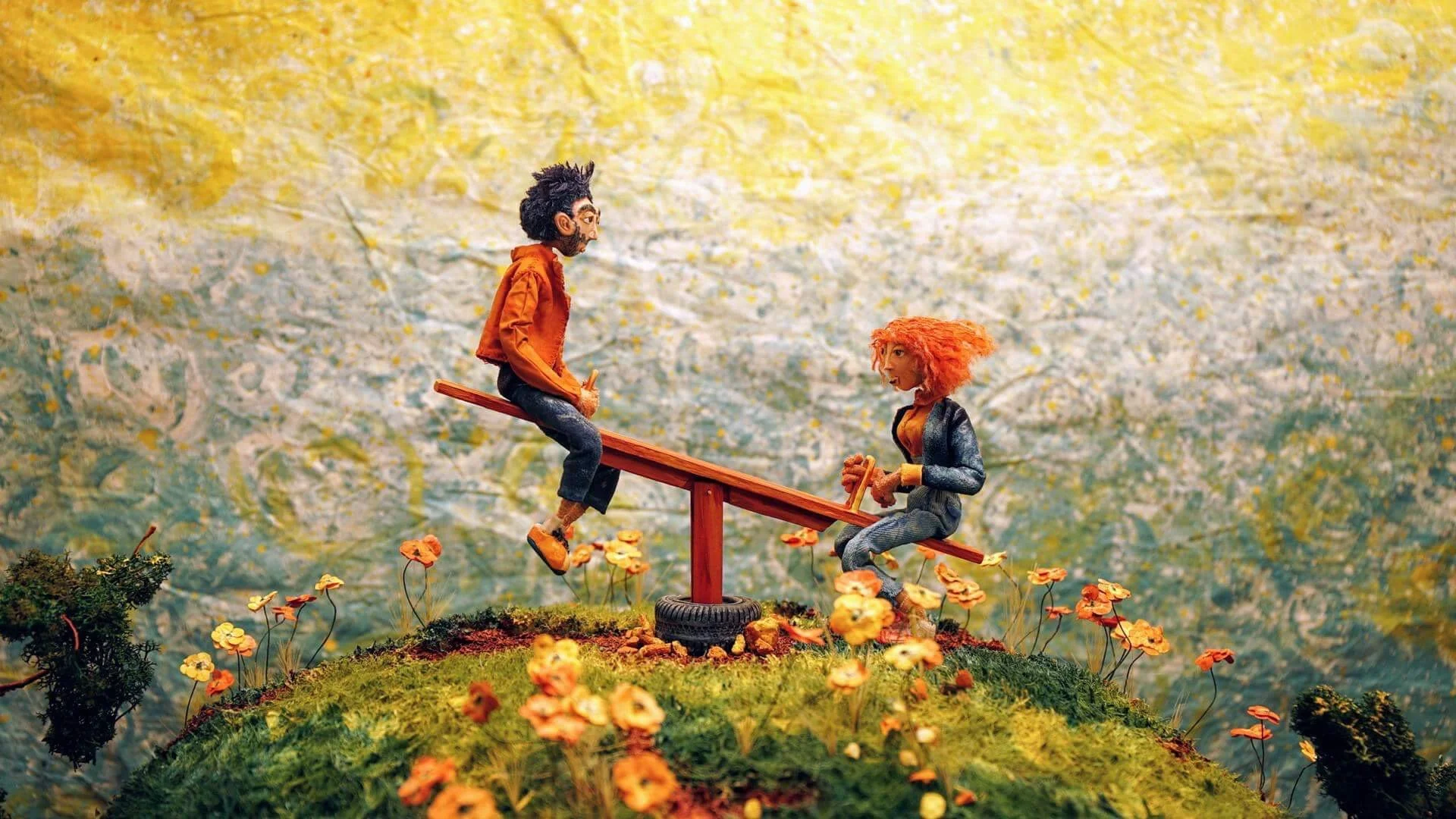 Miniature scene of two handmade puppet figures, a man and a woman, on a seesaw in a garden setting with flowers, against an impressionistic background. Film still from Theo & Celeste short film.