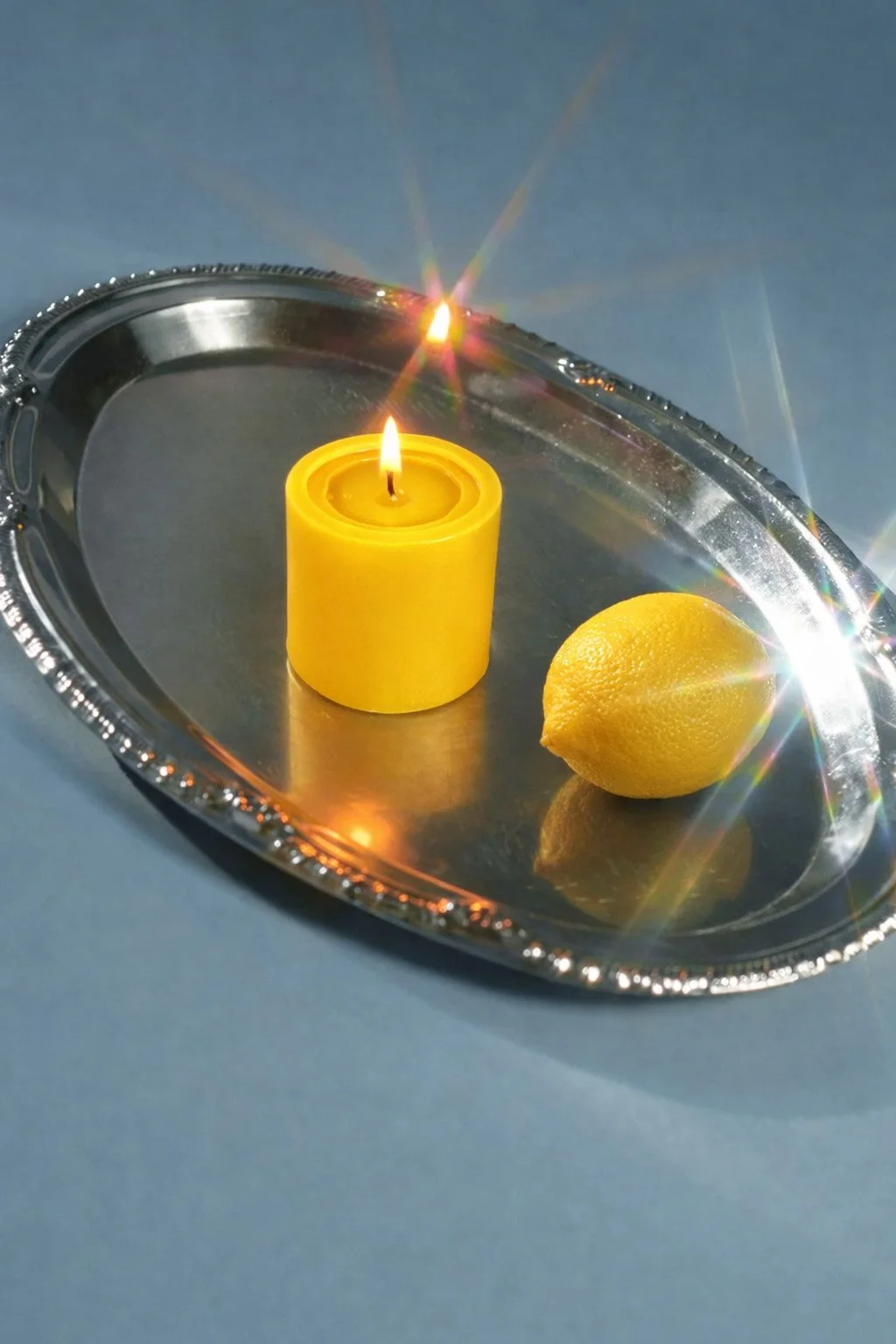 A silver tray with a lit yellow candle and a lemon on a blue surface.