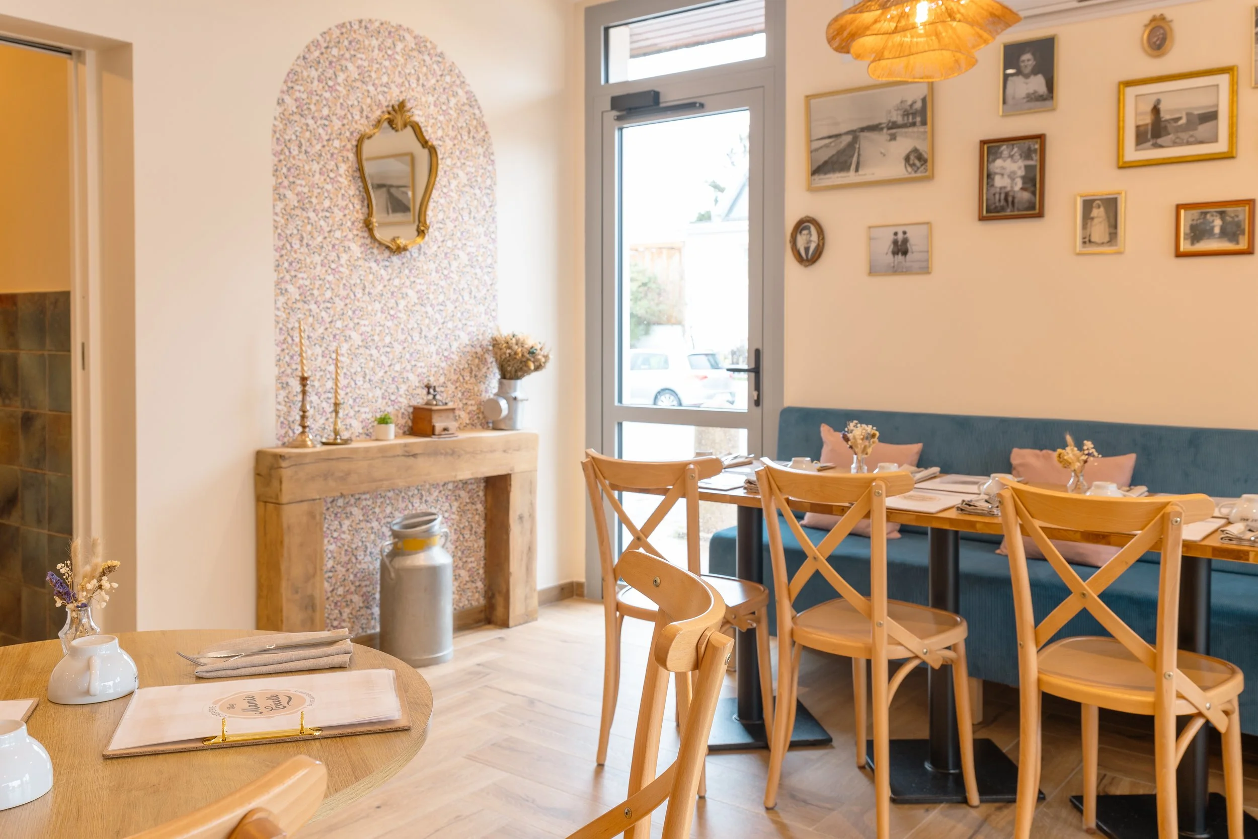 Intérieur d'une salle à manger lumineuse avec une table en bois, chaises en bois, décor moderne, mur avec plusieurs cadres et une porte-fenêtre donnant sur l'extérieur.
